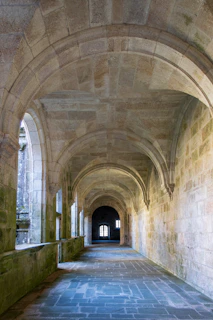 A stone arched corridor with mossy walls and a paved floor in a monastery