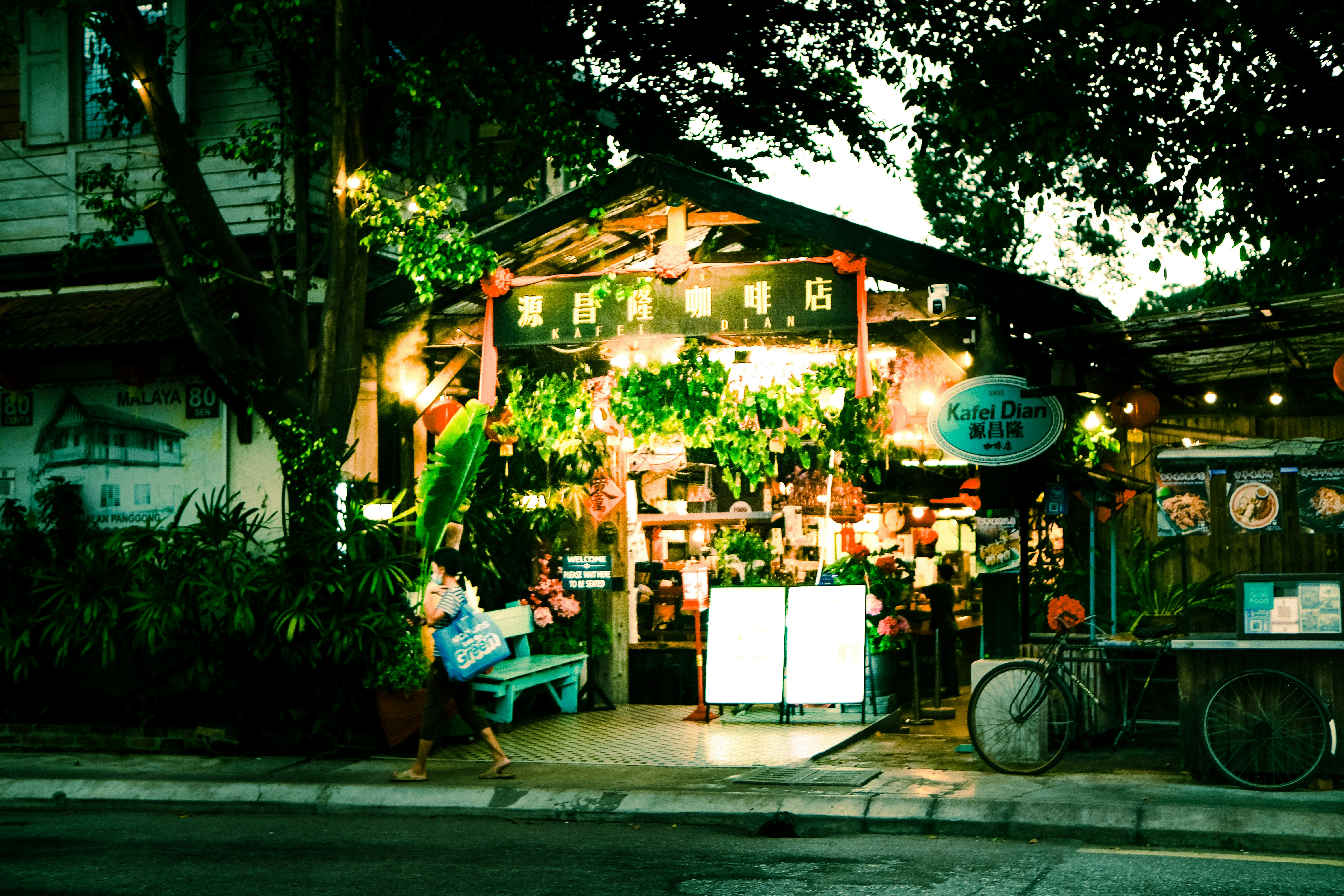 A person walking past a traditional coffee shop with hanging plants and signage