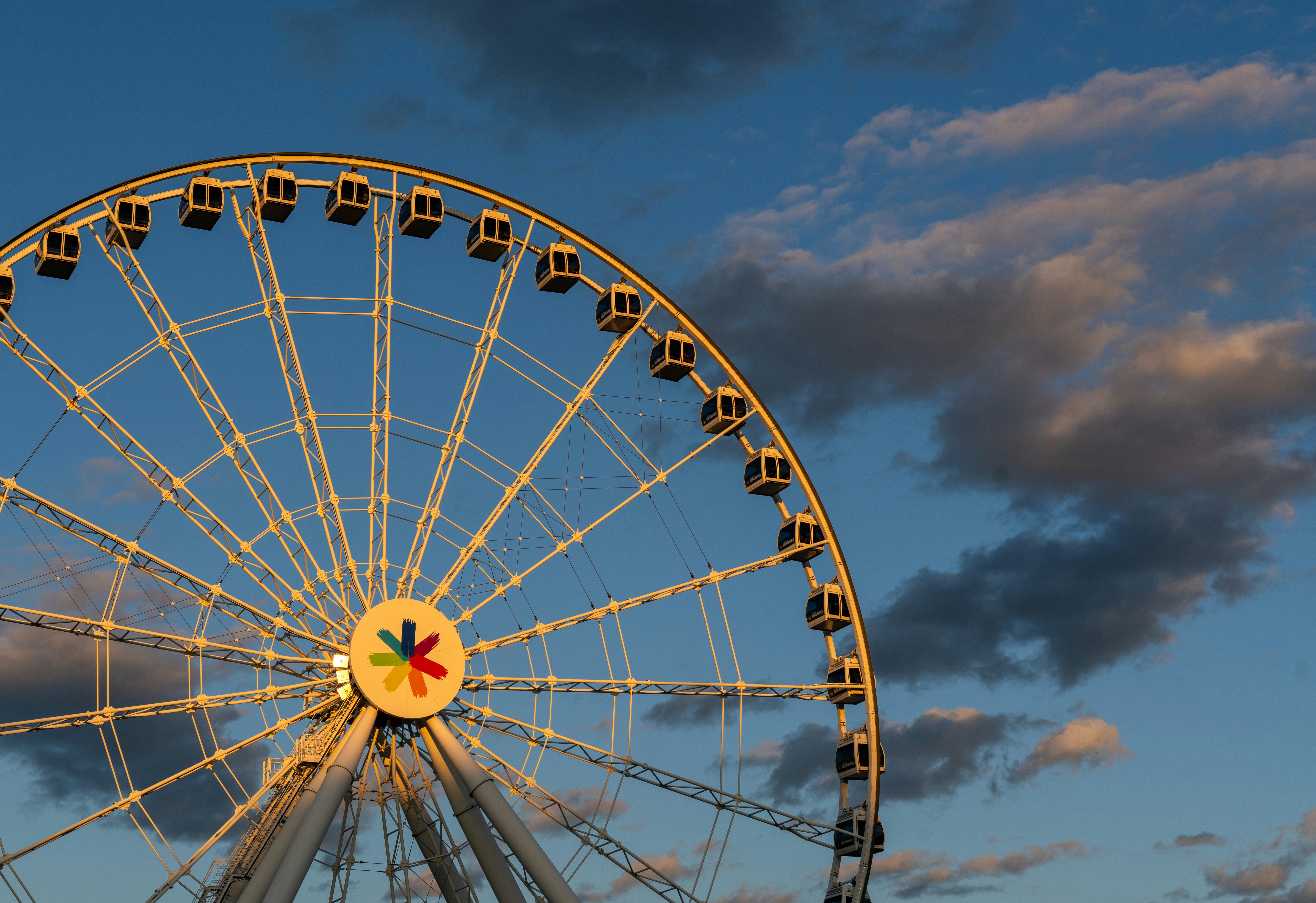 A white ferris wheel against a blue sky with scattered clouds at golden hour