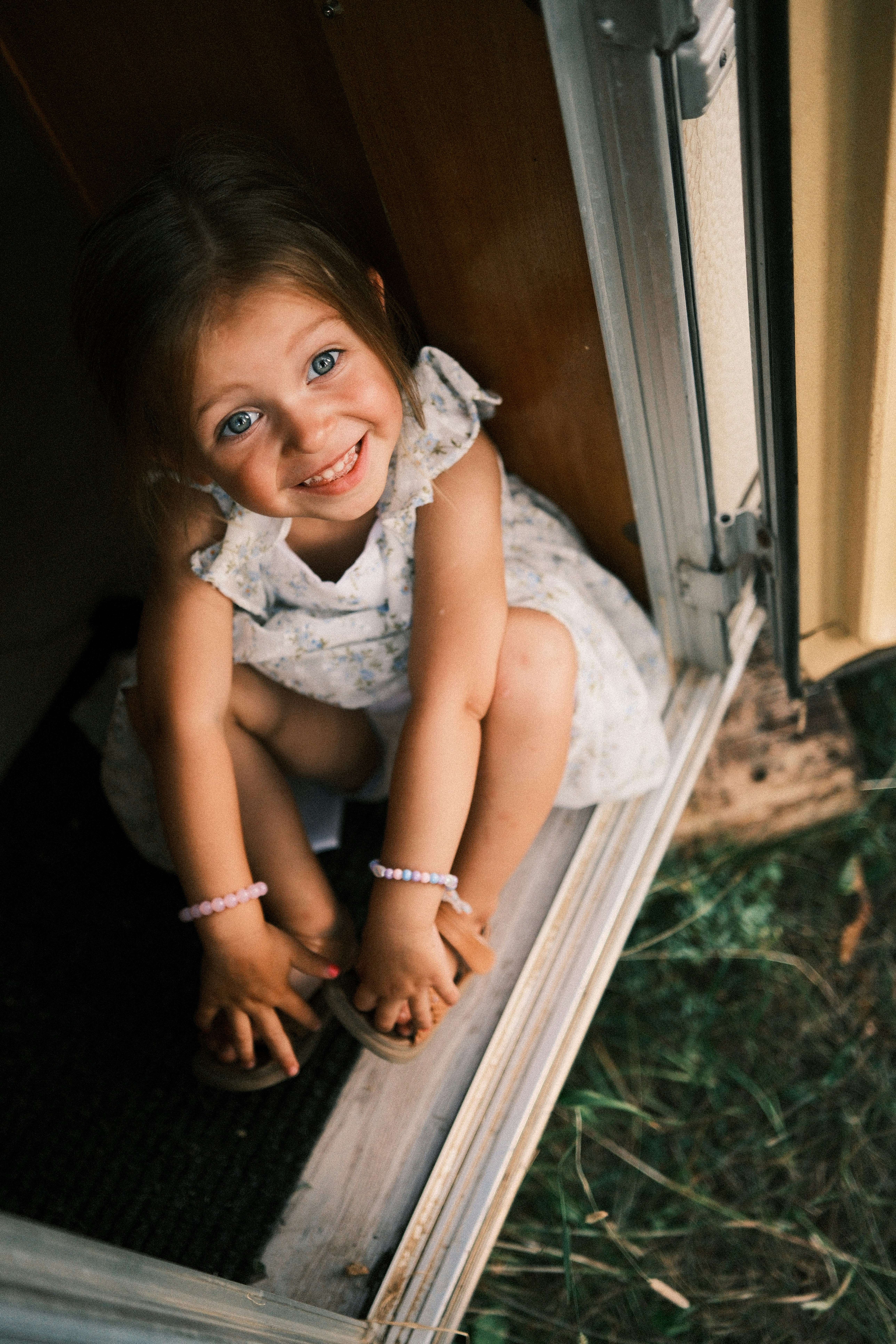 A smiling child in a floral dress sitting in a doorway