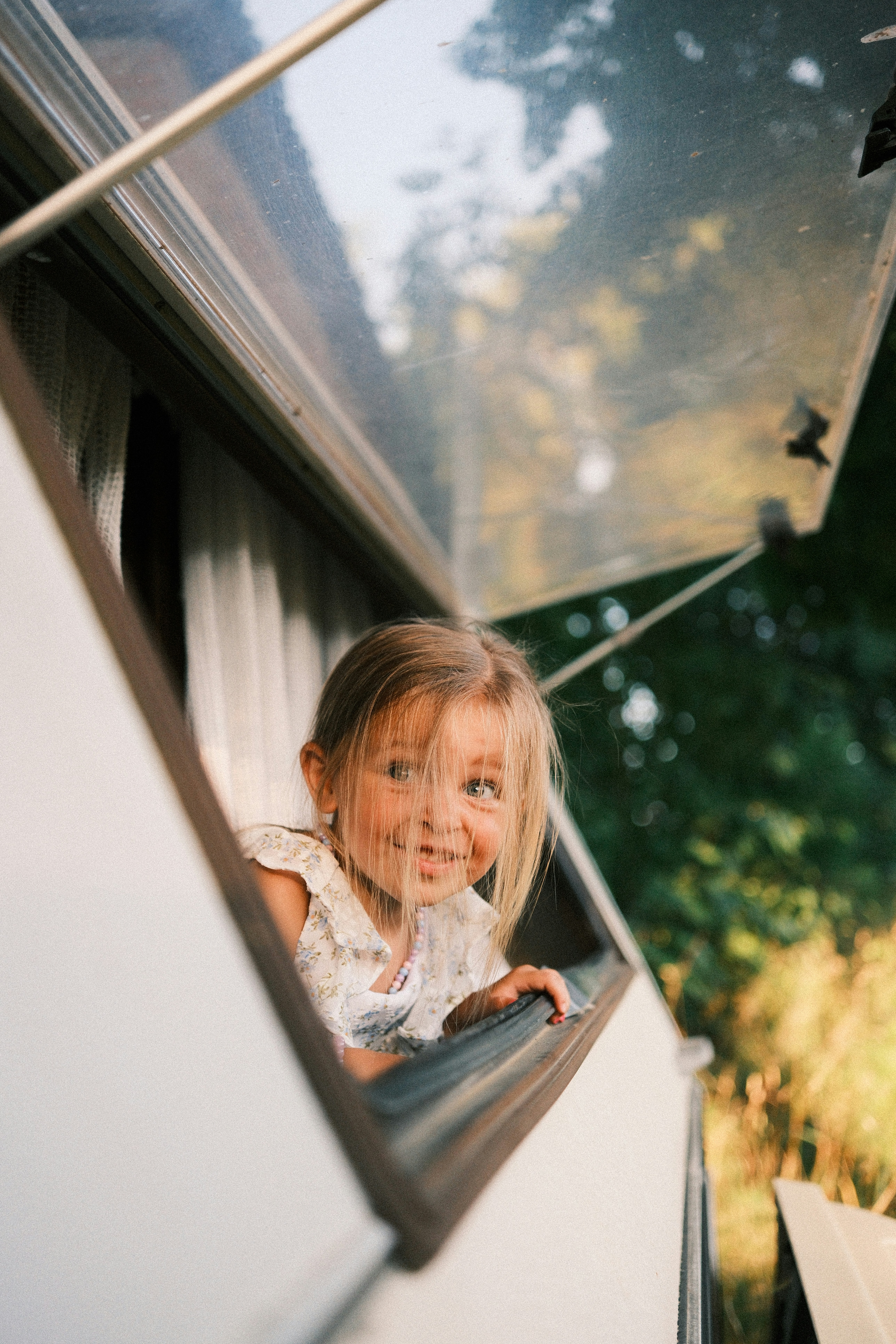 A young child smiling while looking out of an open camper window