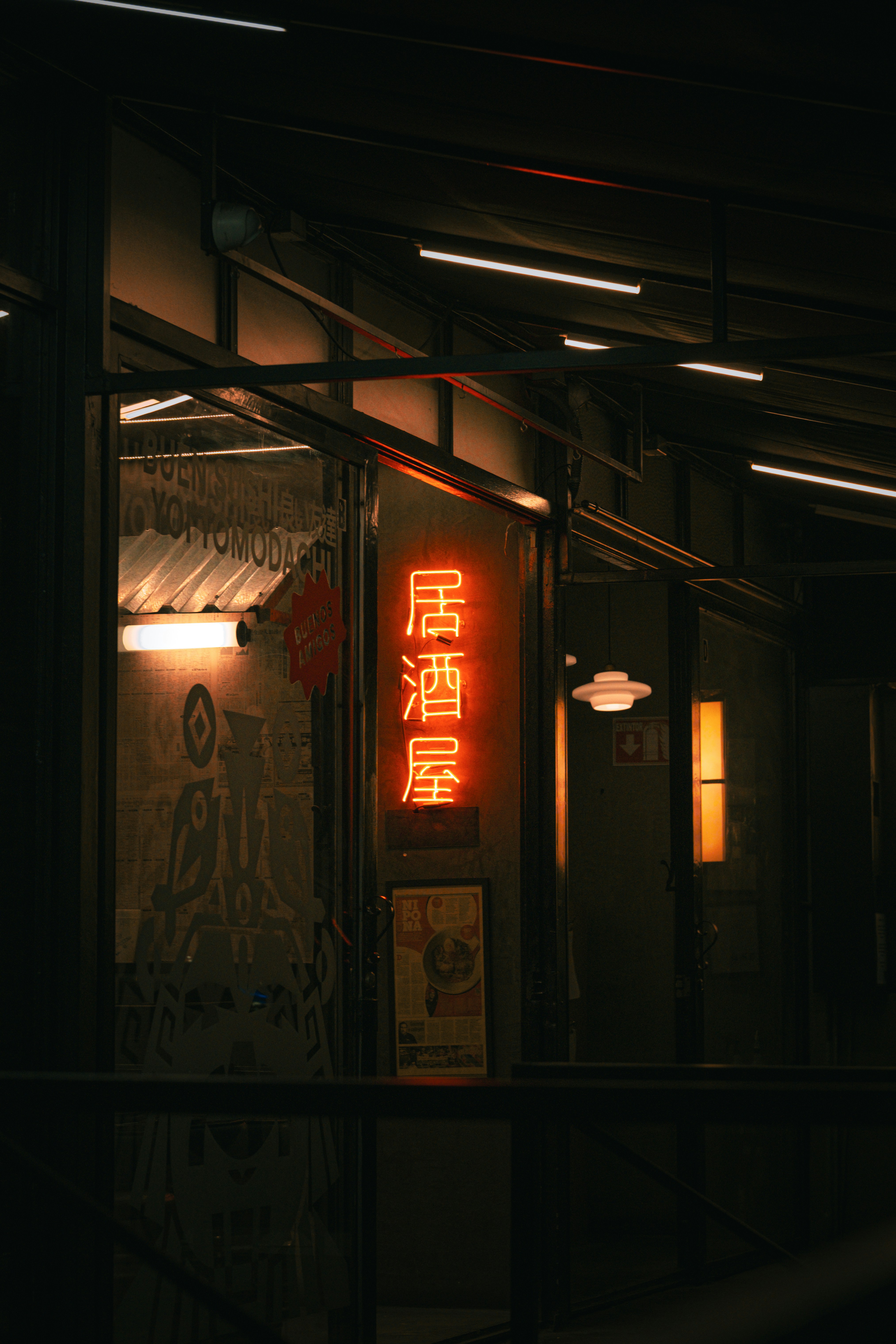 Ein leuchtend orangefarbenes Neonschild in japanischen Schriftzeichen an einer dunklen Restaurantfassade