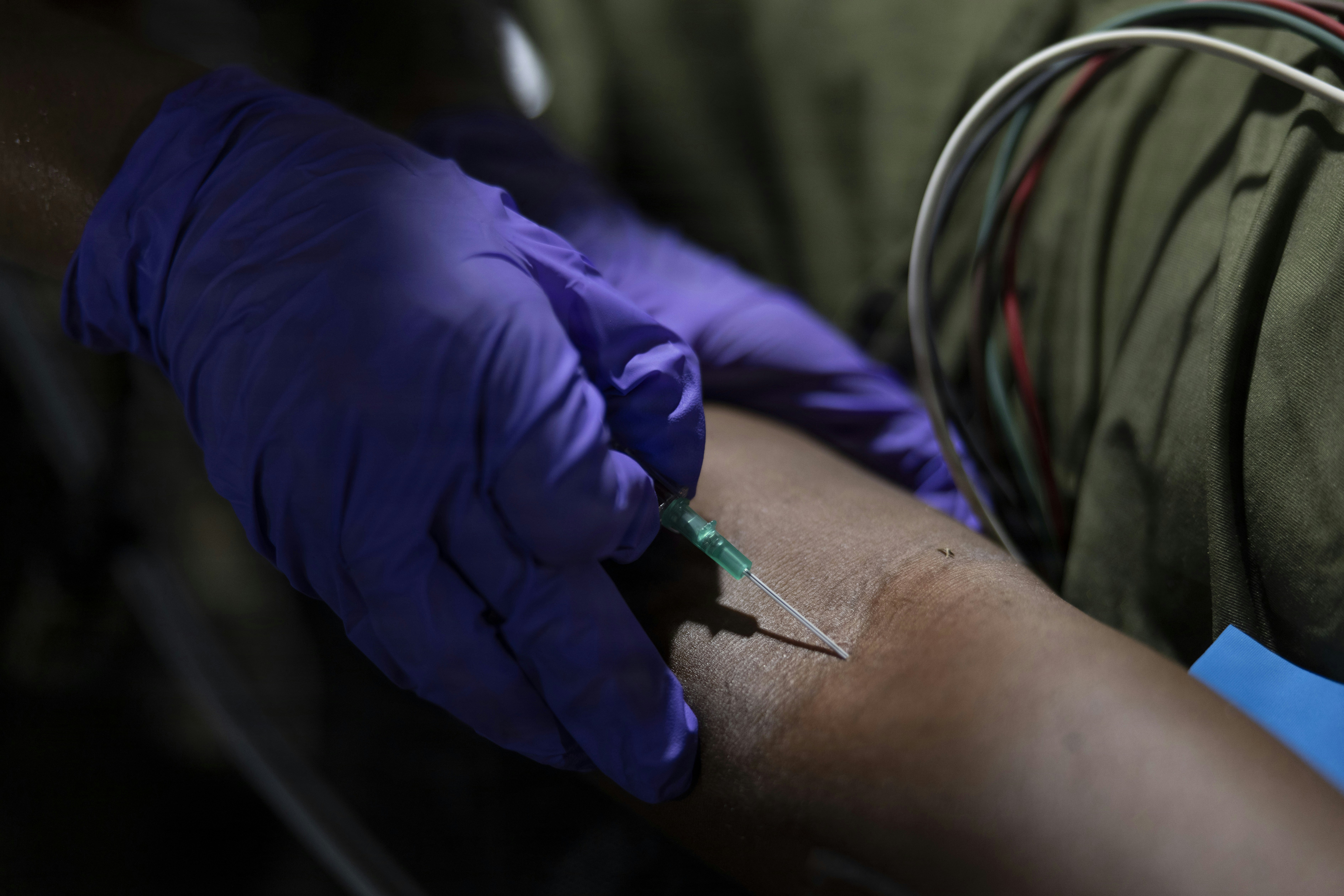 A person in purple gloves inserting a needle into a patient's arm