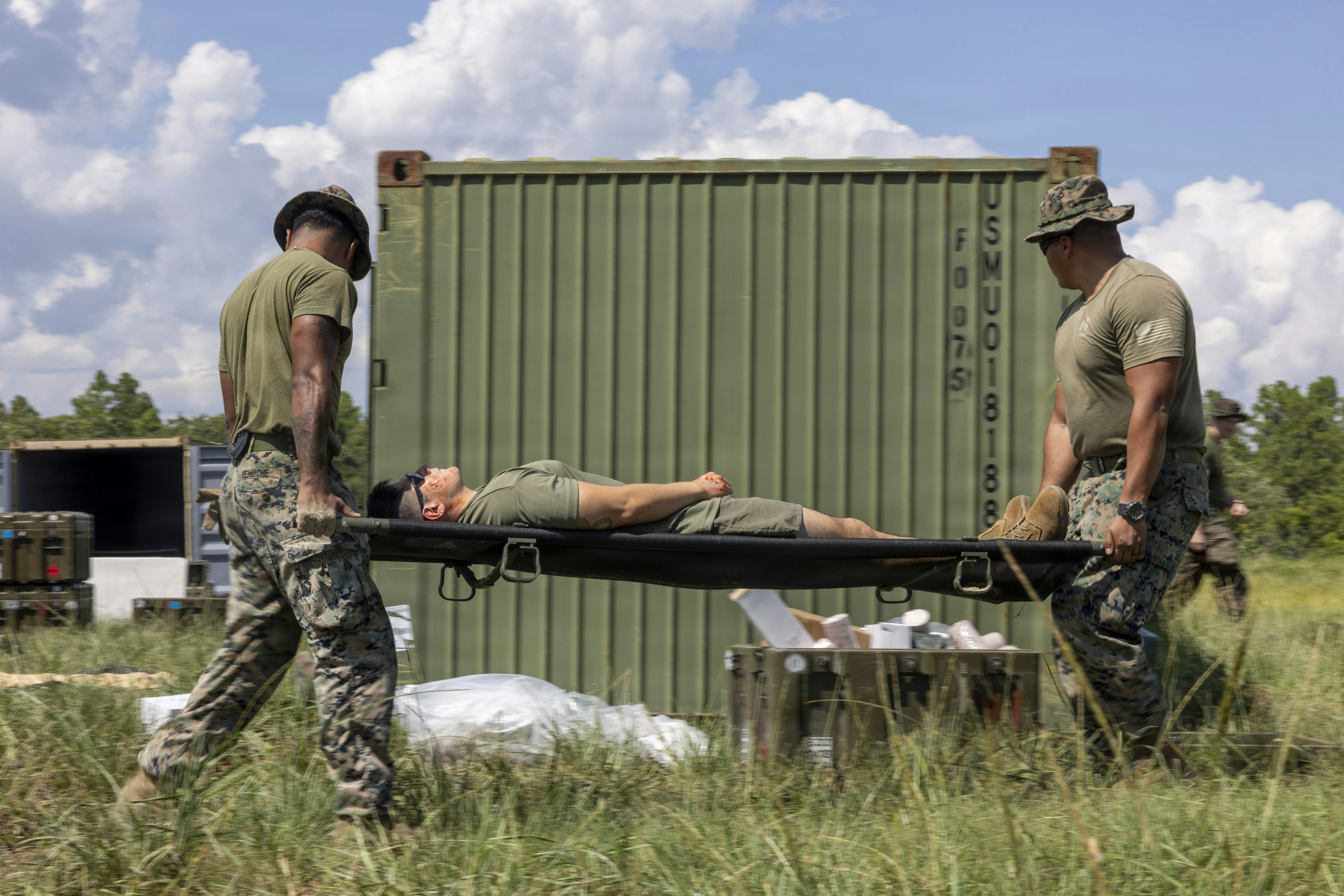 Two soldiers in camouflage uniforms carrying a person on a stretcher outdoors