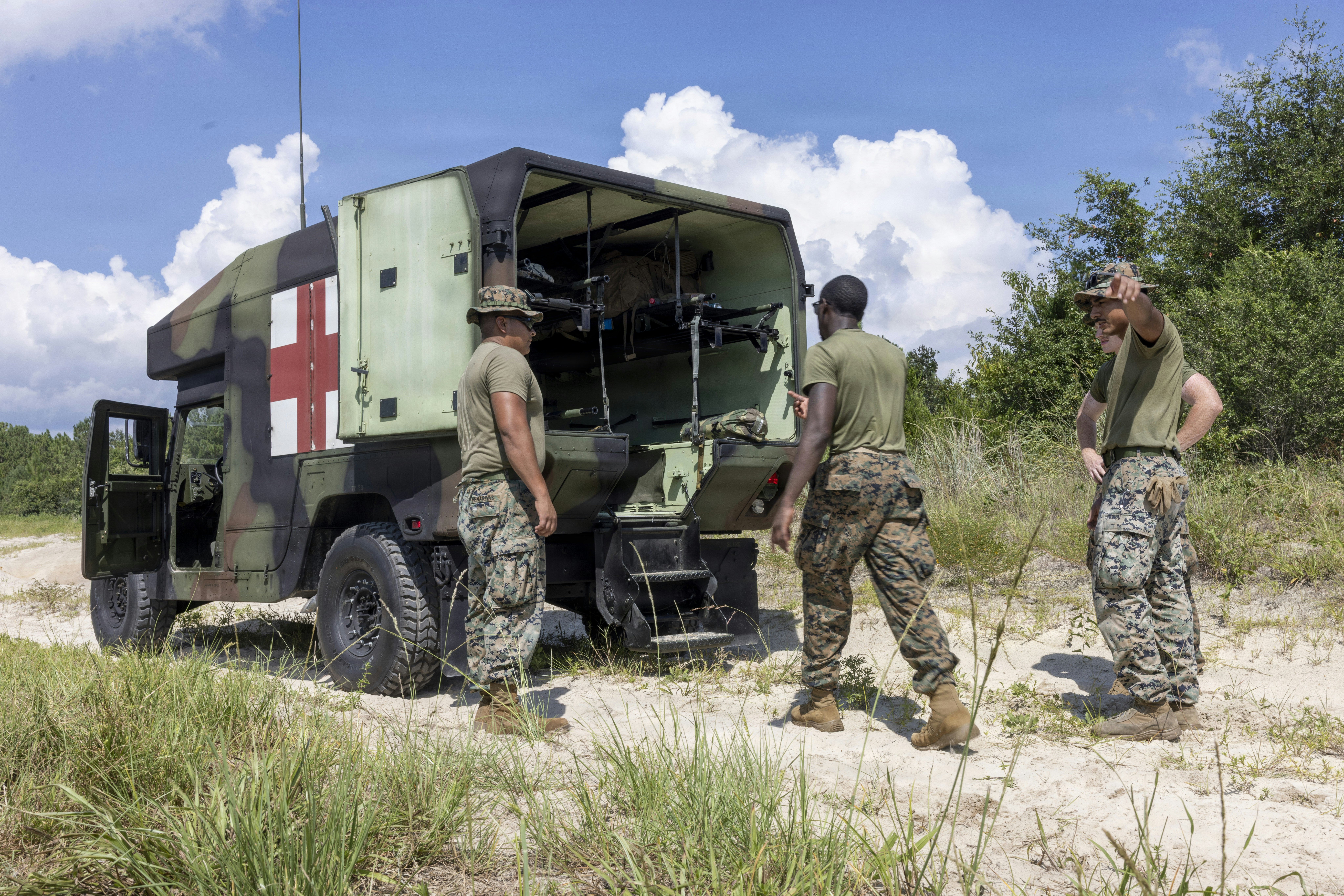 Three soldiers in camouflage uniforms standing by an open military ambulance in a field