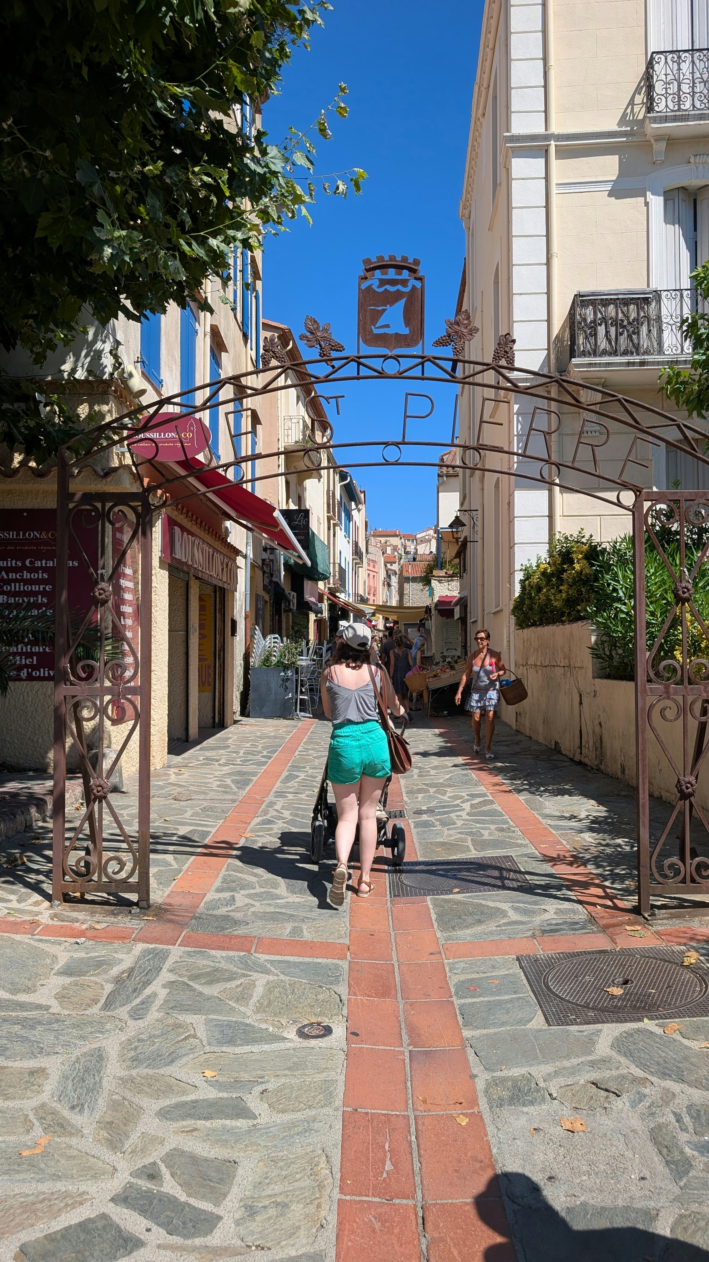 A person pushing a stroller through a stone archway on a sunny street