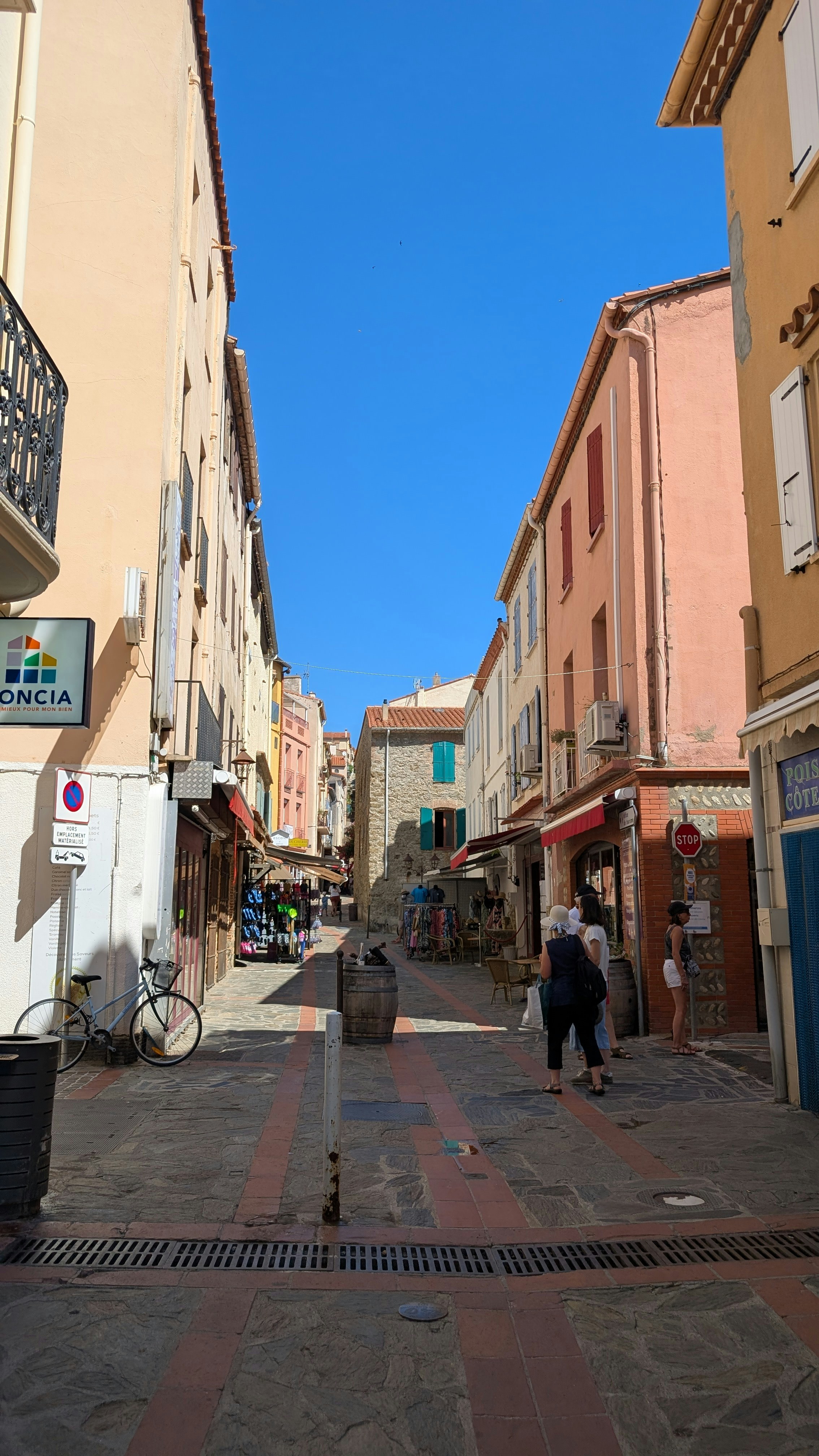 People walking along a narrow stone street lined with colorful buildings and shops
