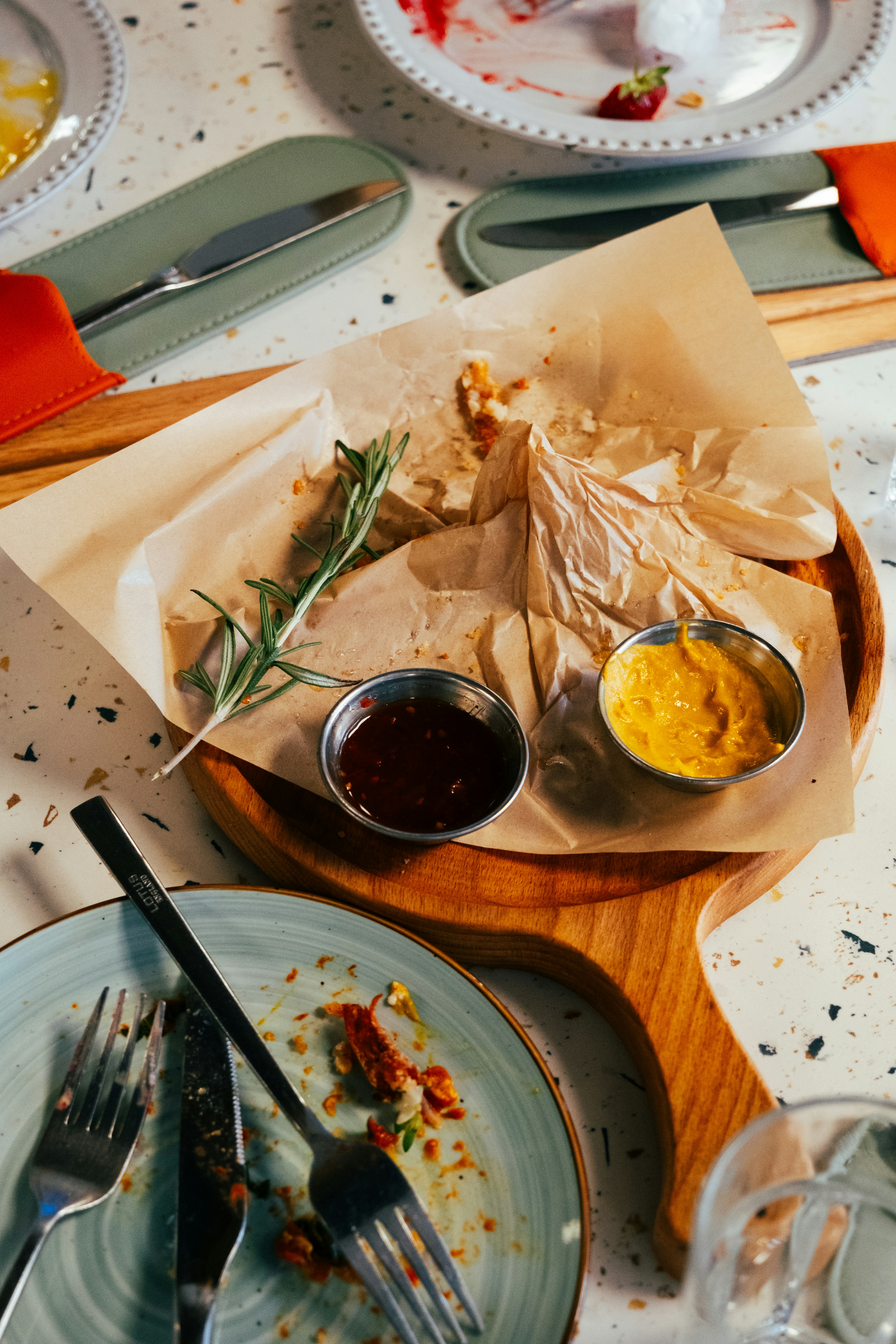 Empty food wrappers and two small metal bowls of sauce on a wooden board