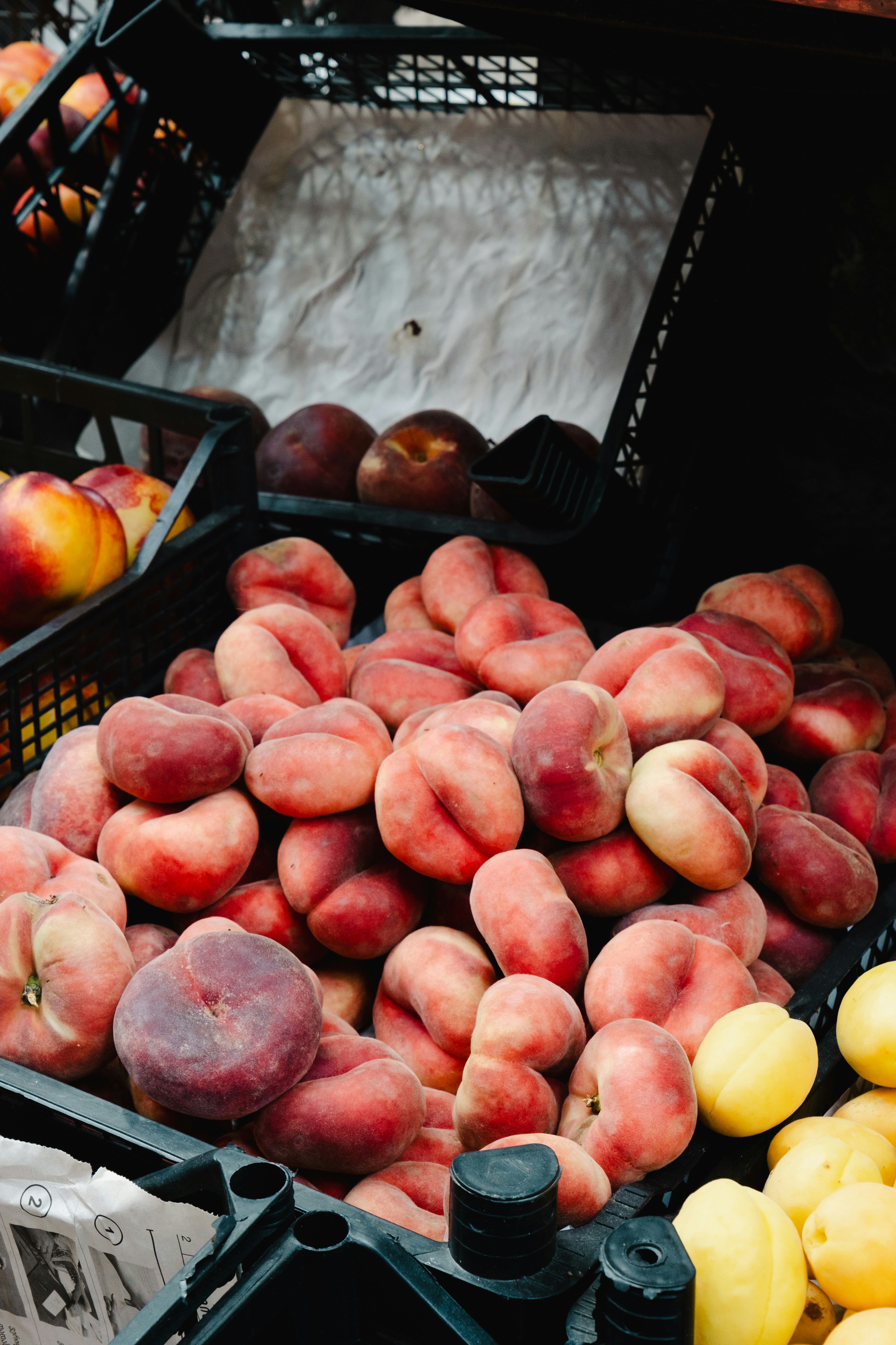 A pile of flat donut peaches in a black plastic crate at a market