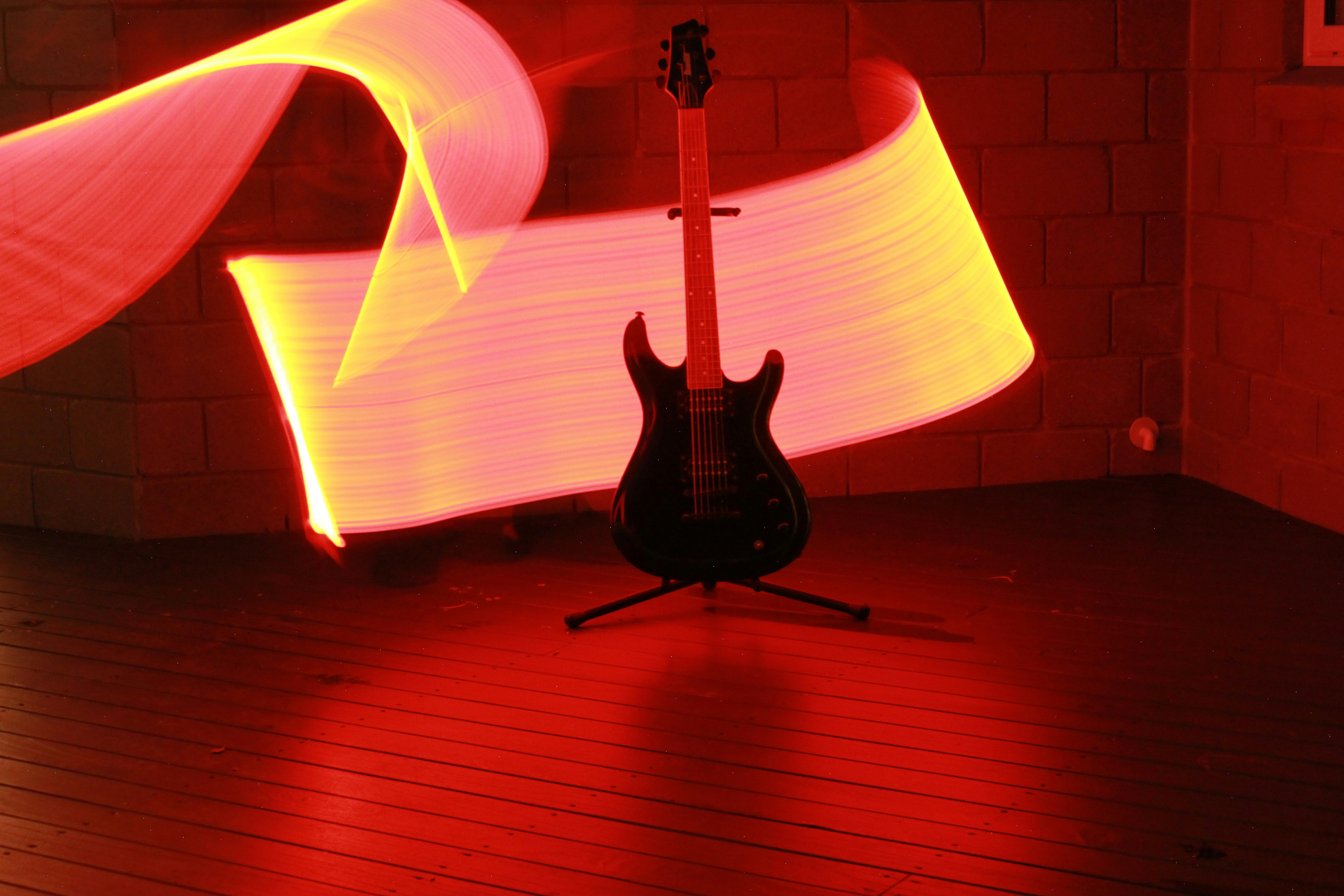 A black electric guitar on a stand with long exposure red light trails
