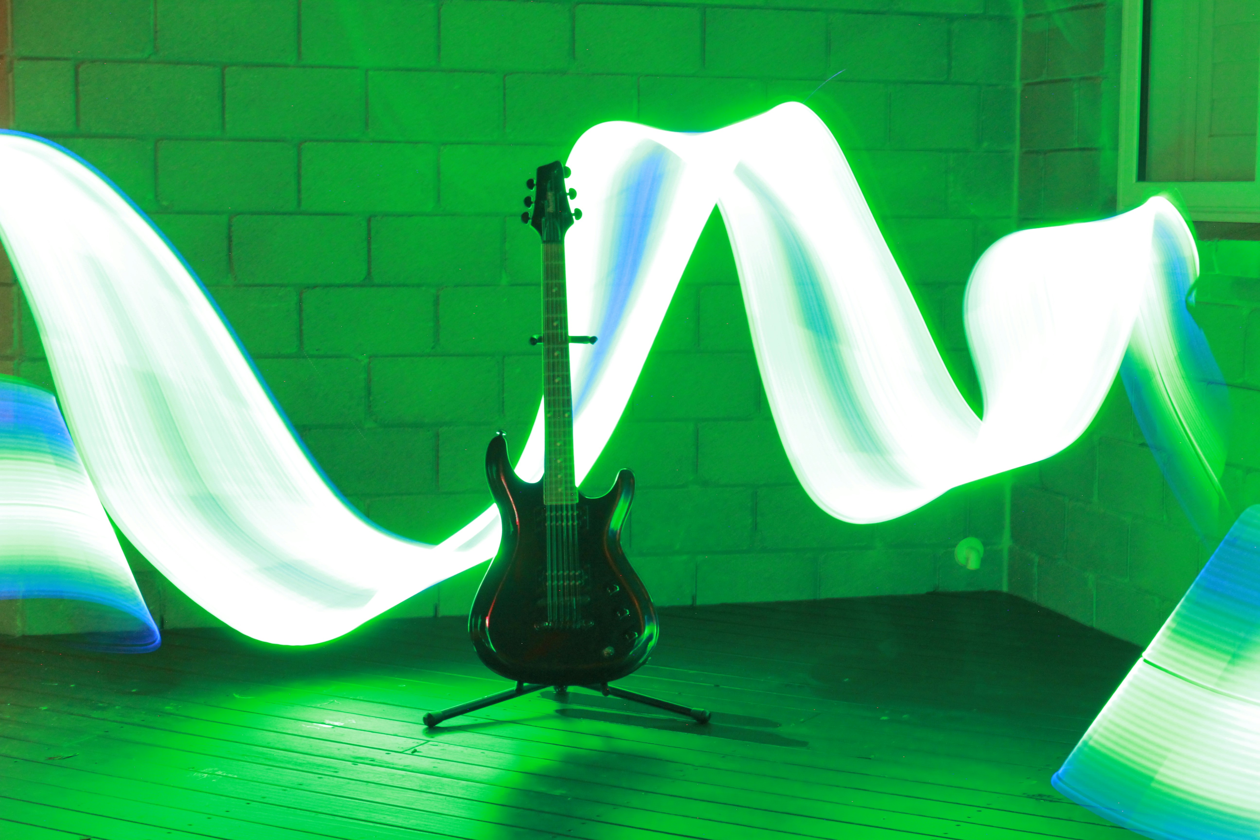 An electric guitar on a stand against a wall with green light painting