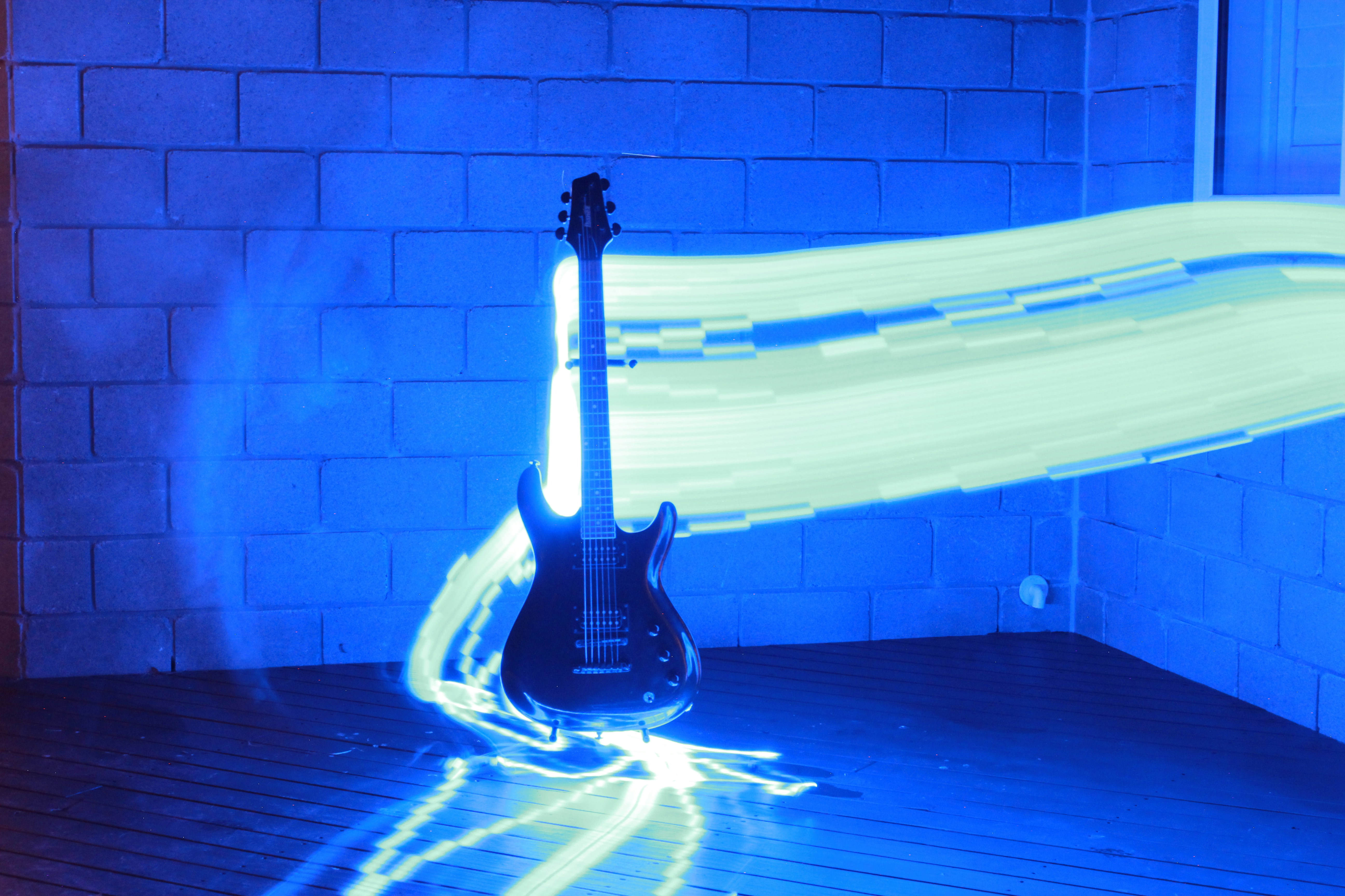An electric guitar silhouetted against a blue brick wall with long exposure light trails