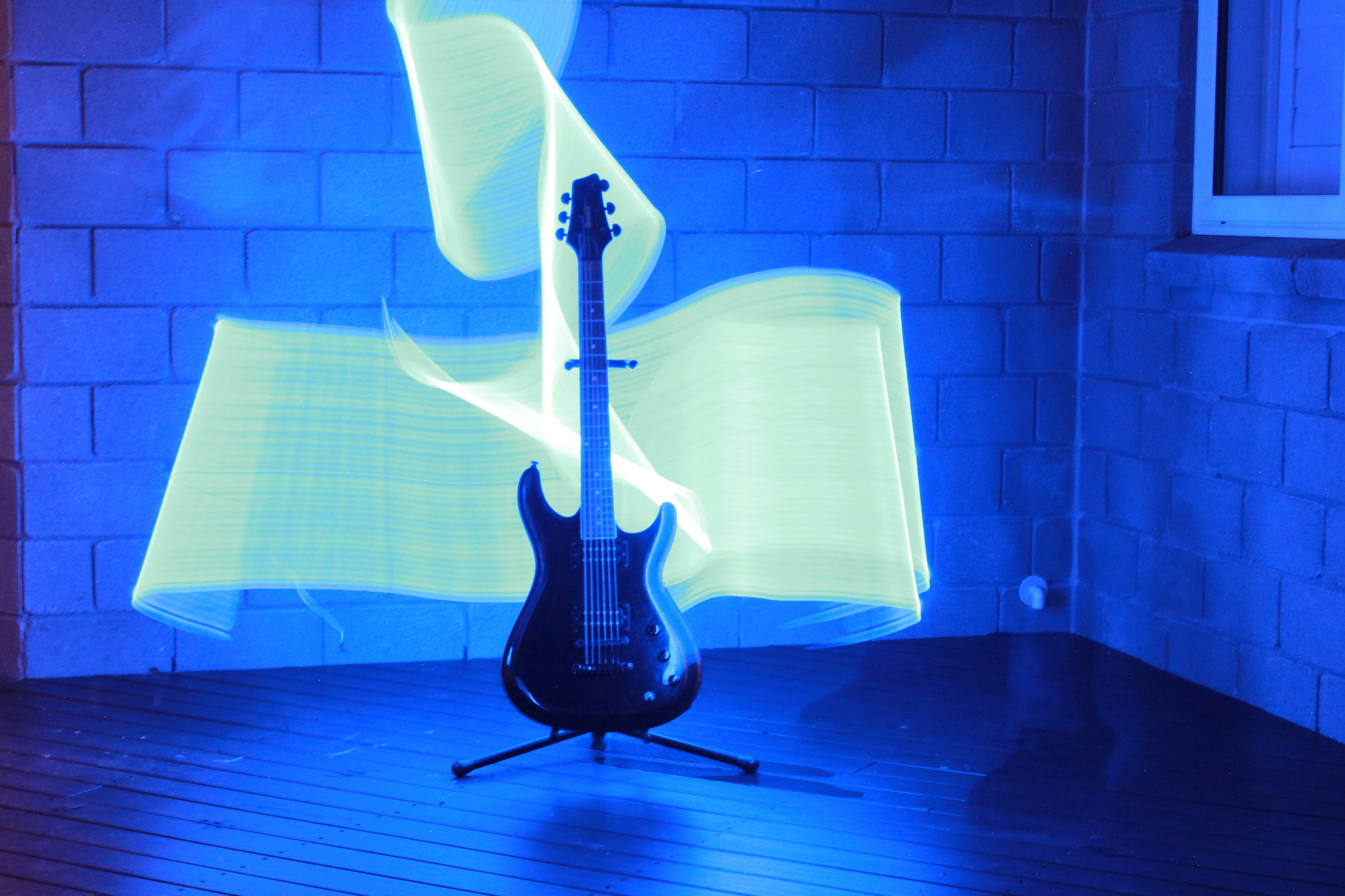 An electric guitar on a stand against a blue wall with yellow light trails
