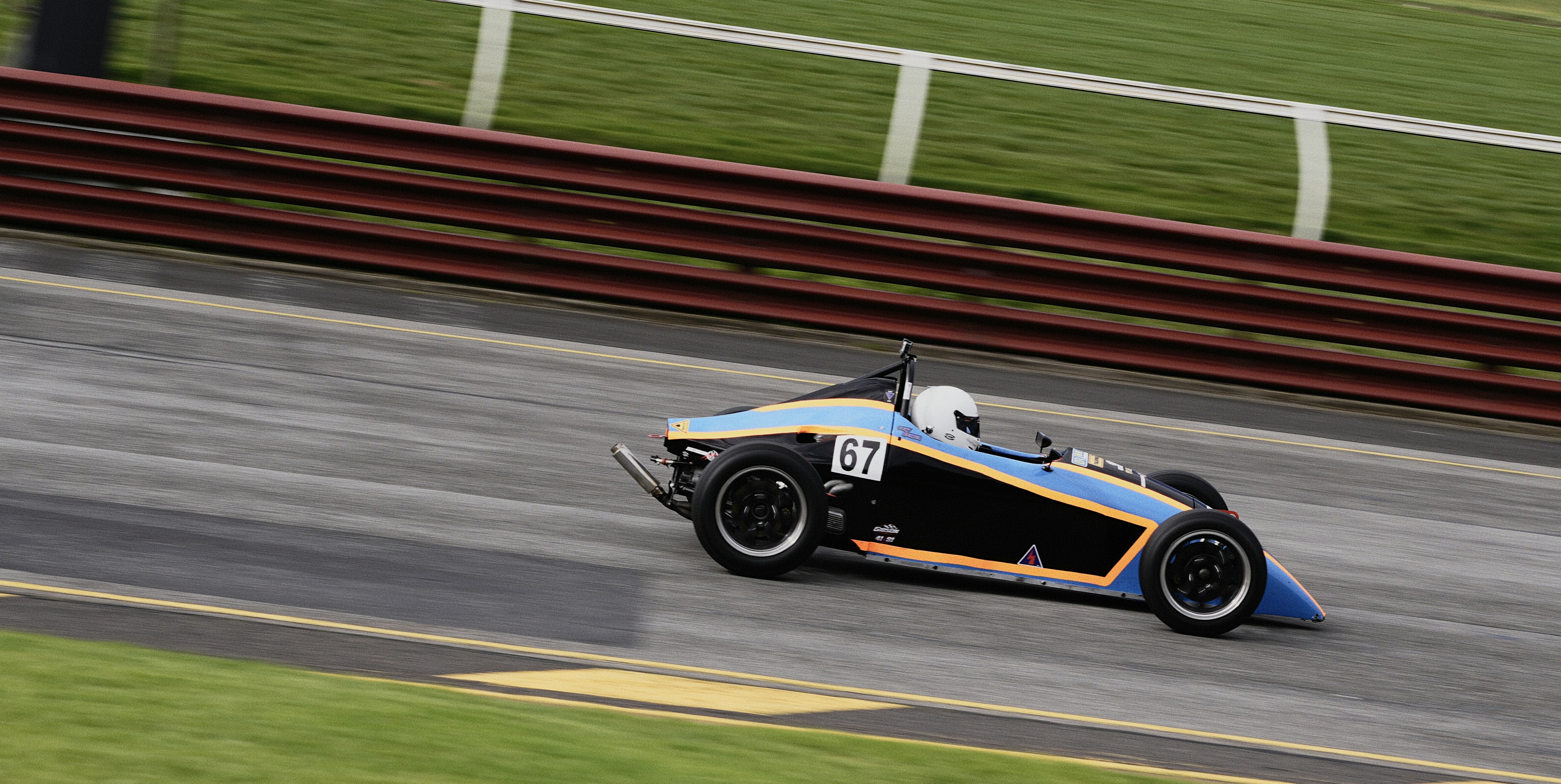 A formula race car with number 67 speeding along a paved track