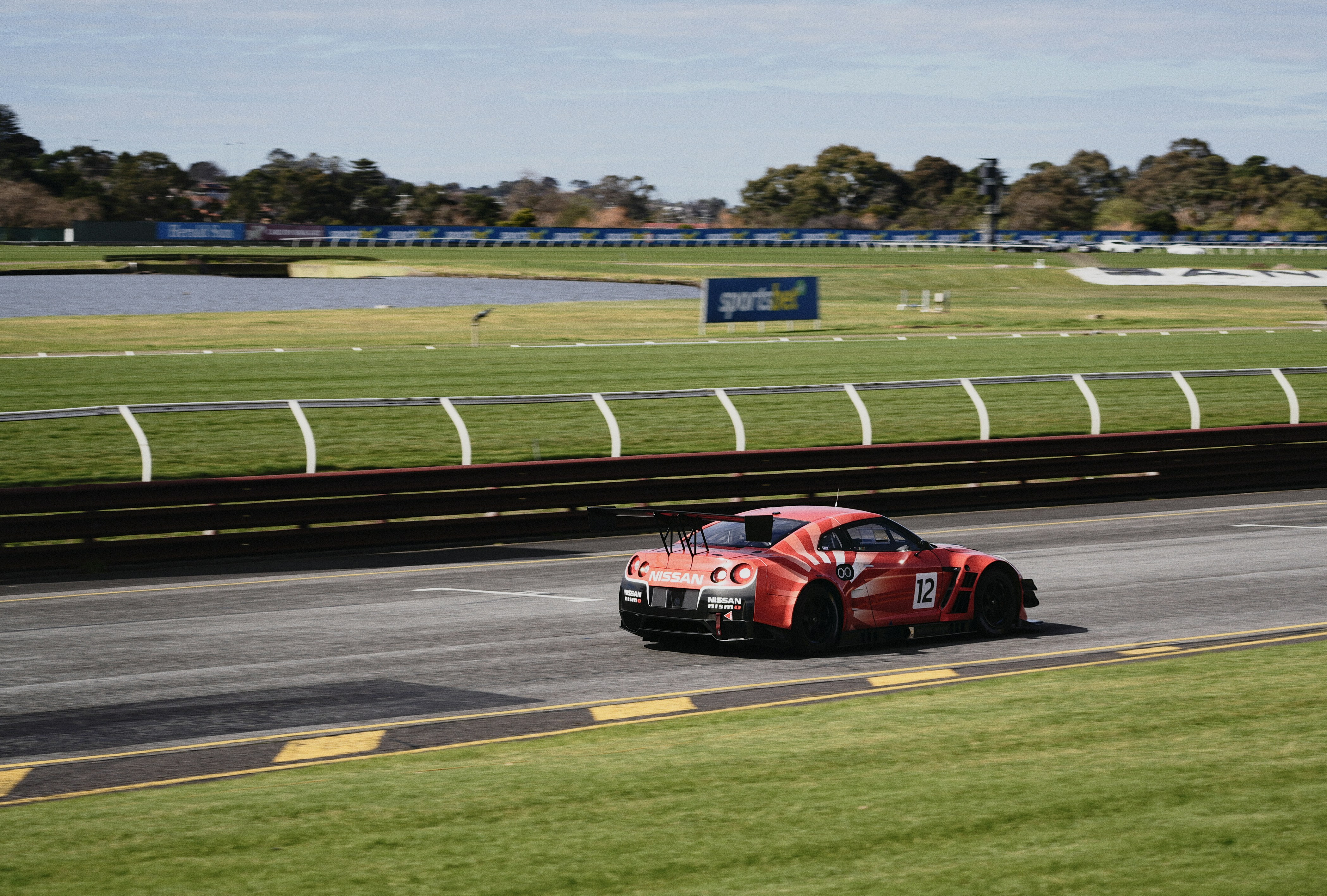 A red Nissan GT-R race car driving on a paved track near grass