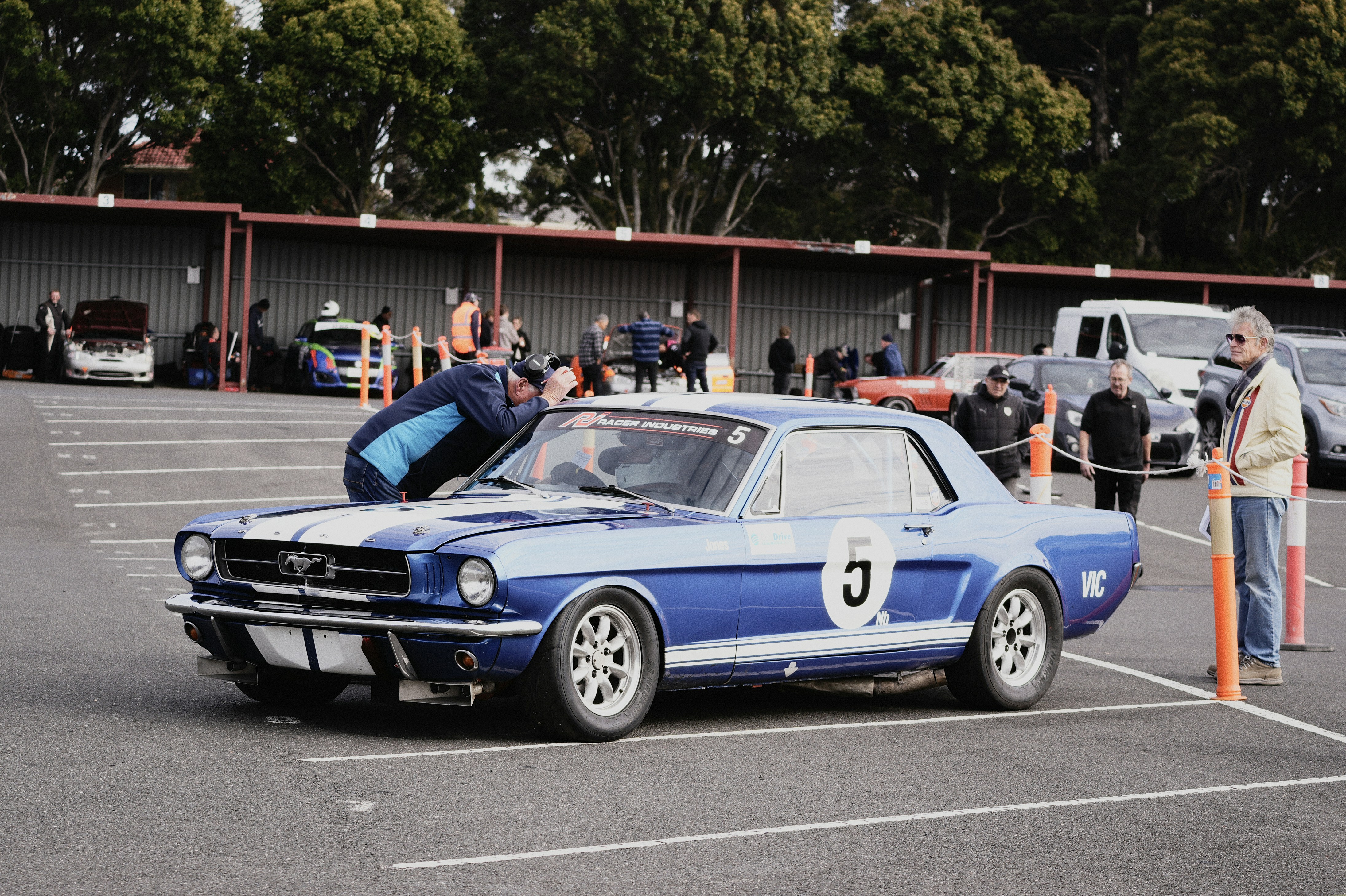 A blue vintage Ford Mustang race car with white stripes in a parking lot