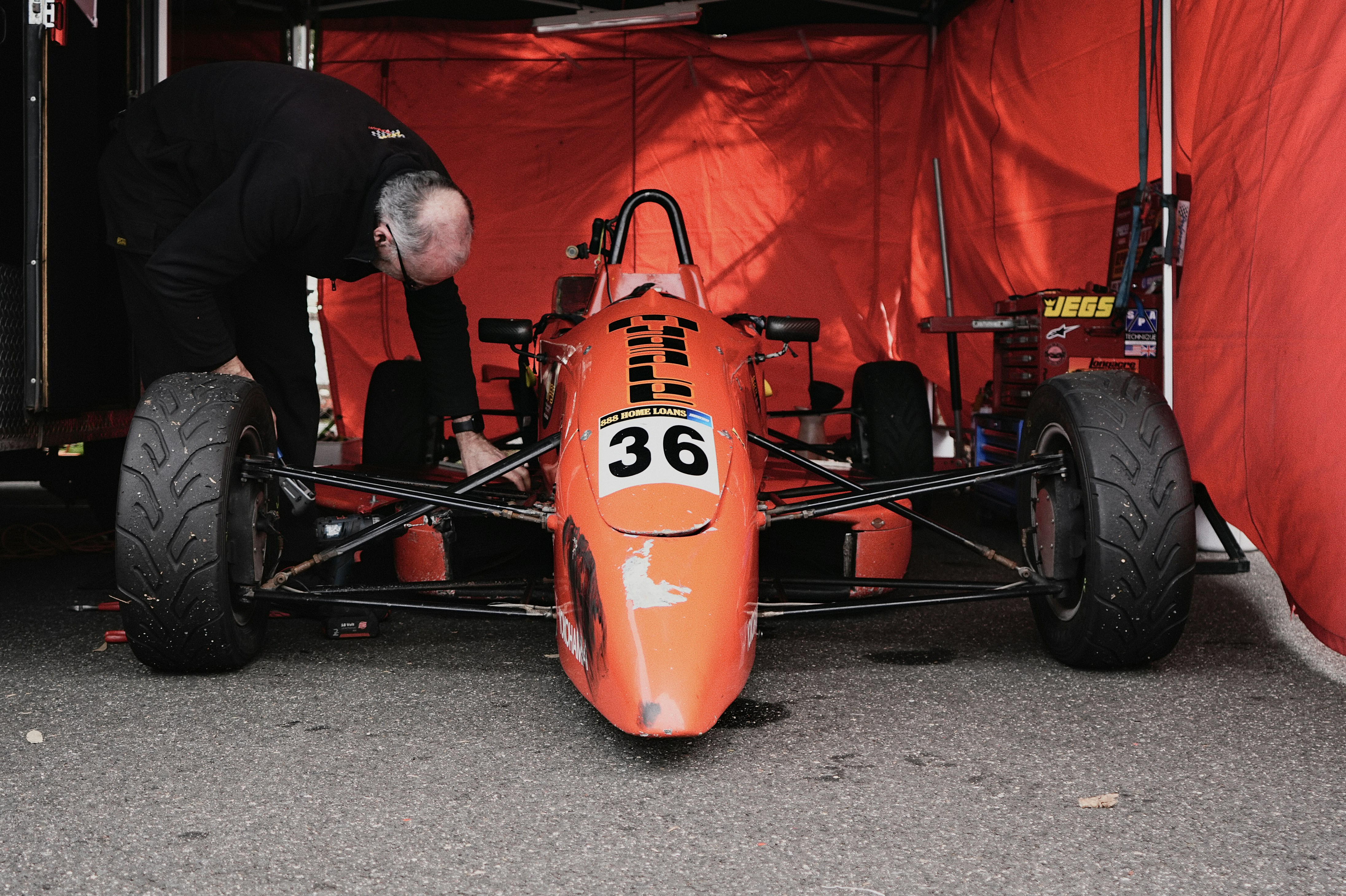 A person working on an orange formula race car inside a red tent