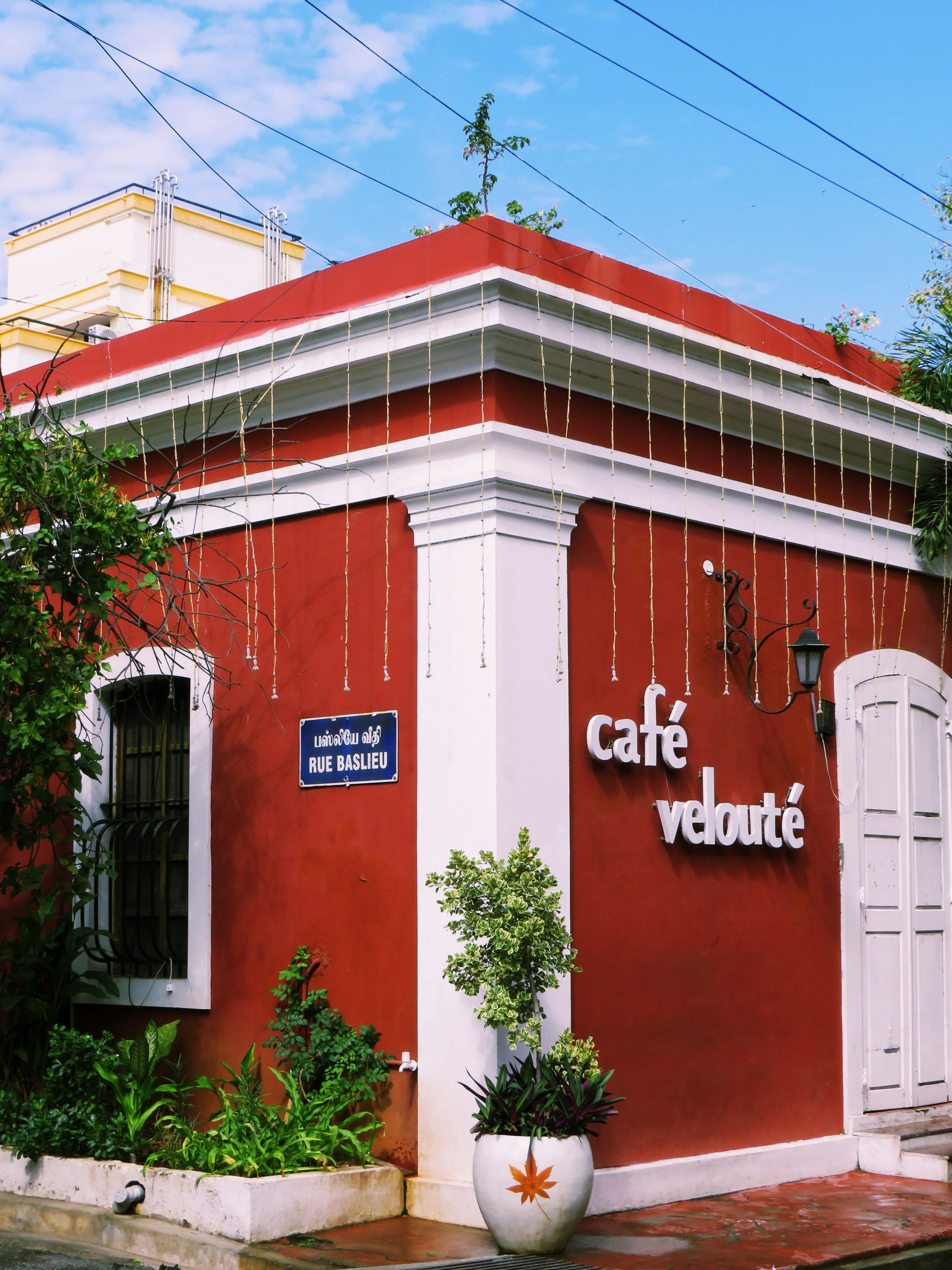 A red cafe building with white trim and a Rue Baslieu street sign