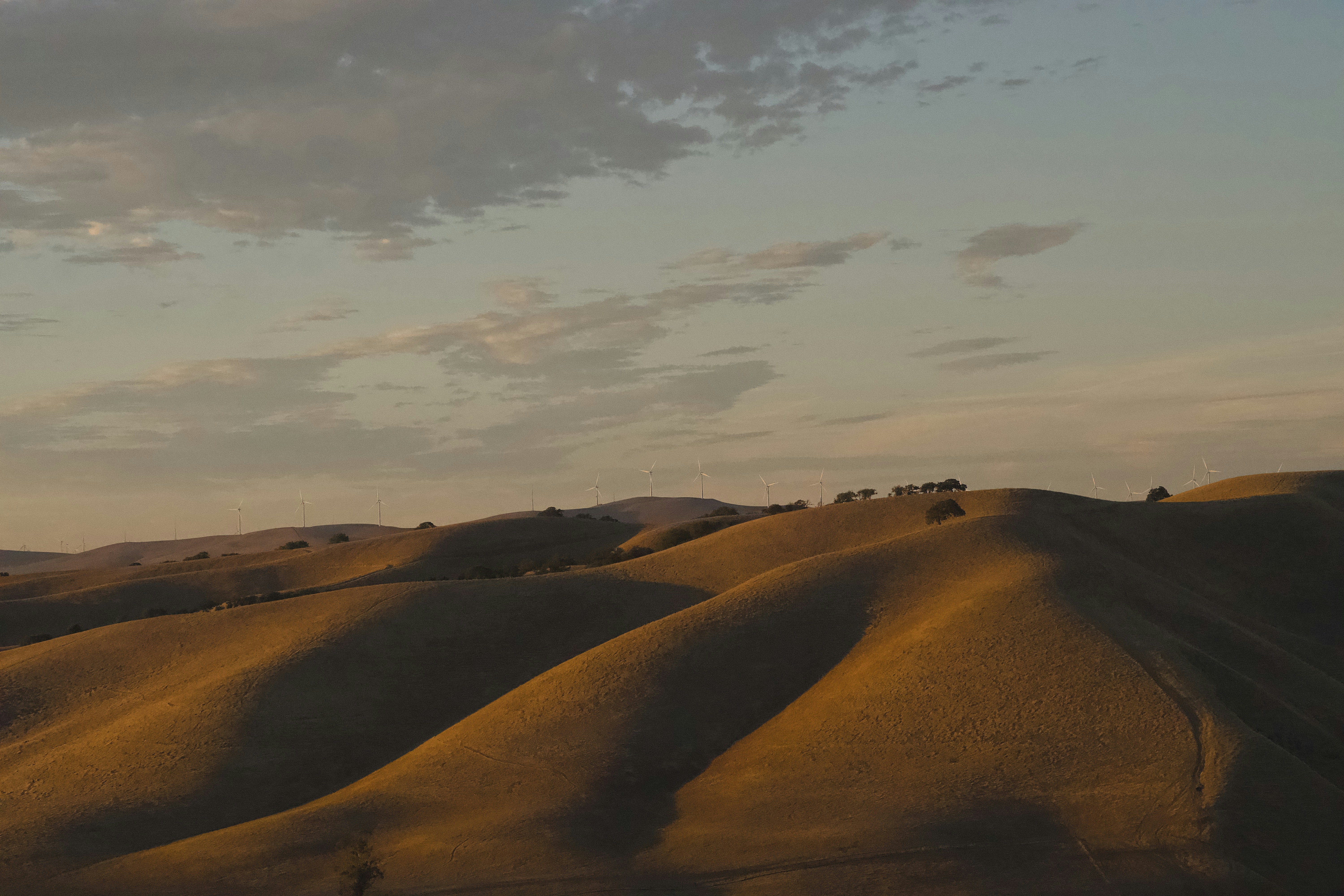Wind turbines on rolling golden hills under a soft evening sky