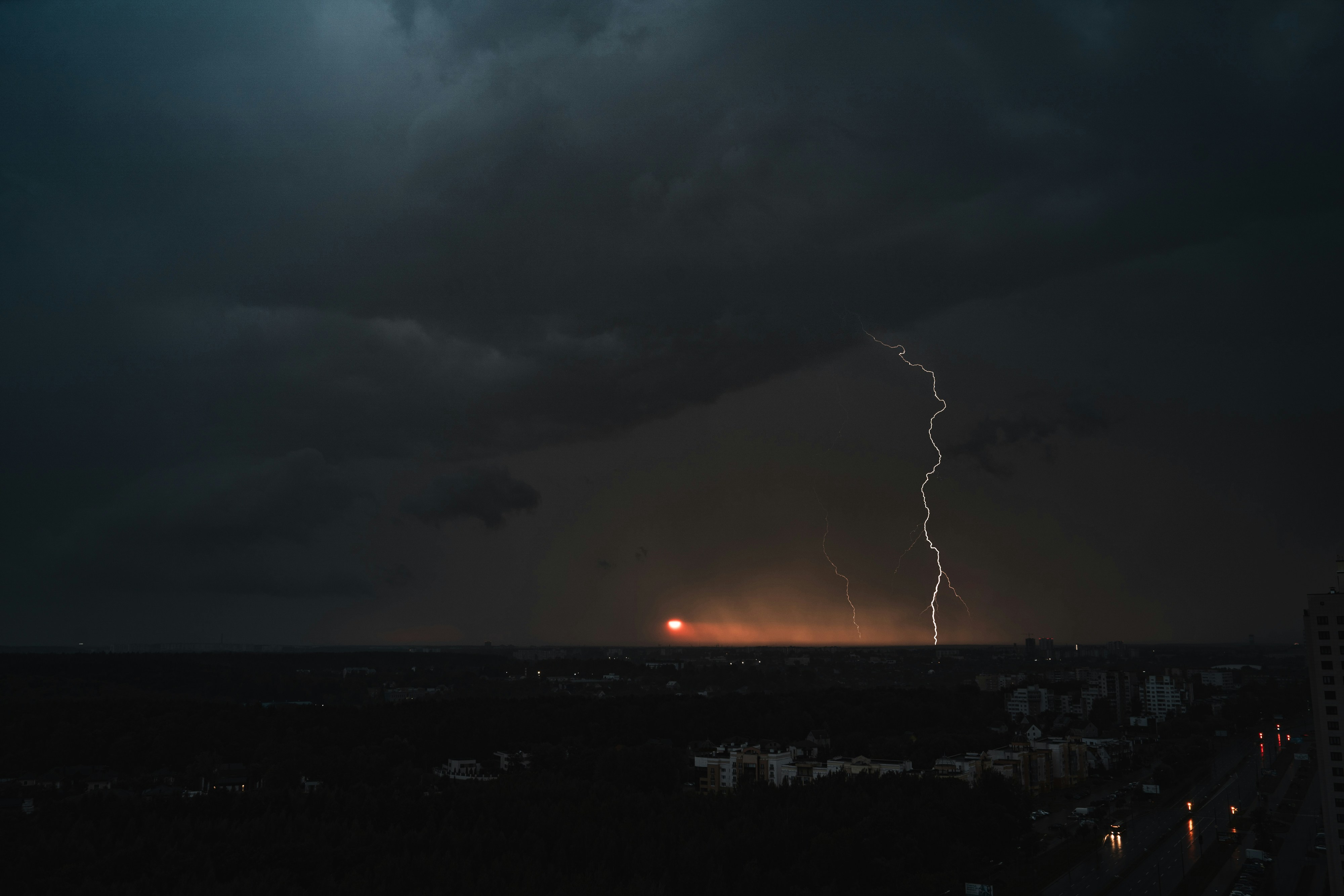 A bright lightning bolt striking the horizon under dark storm clouds at night