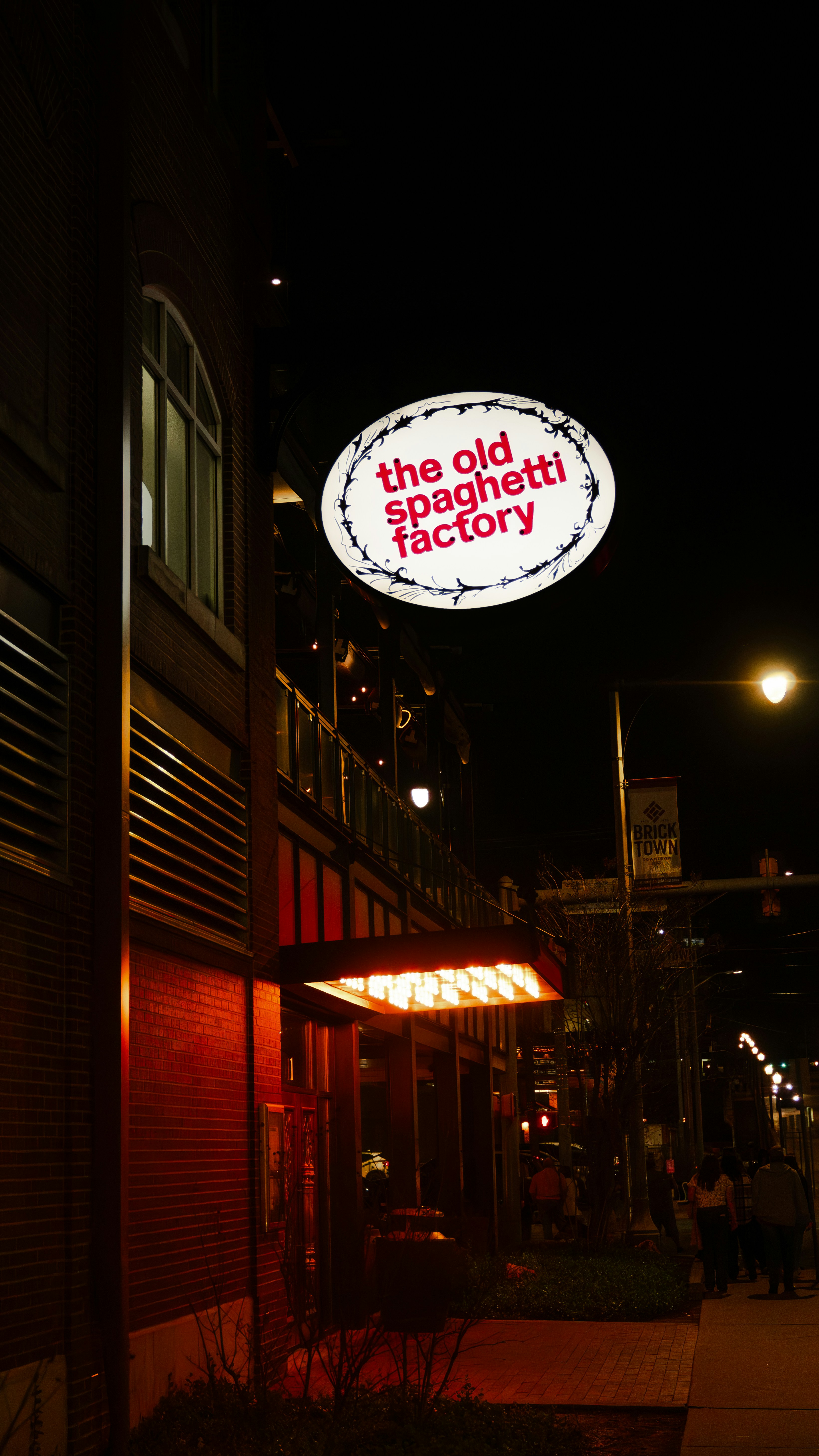A glowing oval sign reading "the old spaghetti factory" above a brick building at night