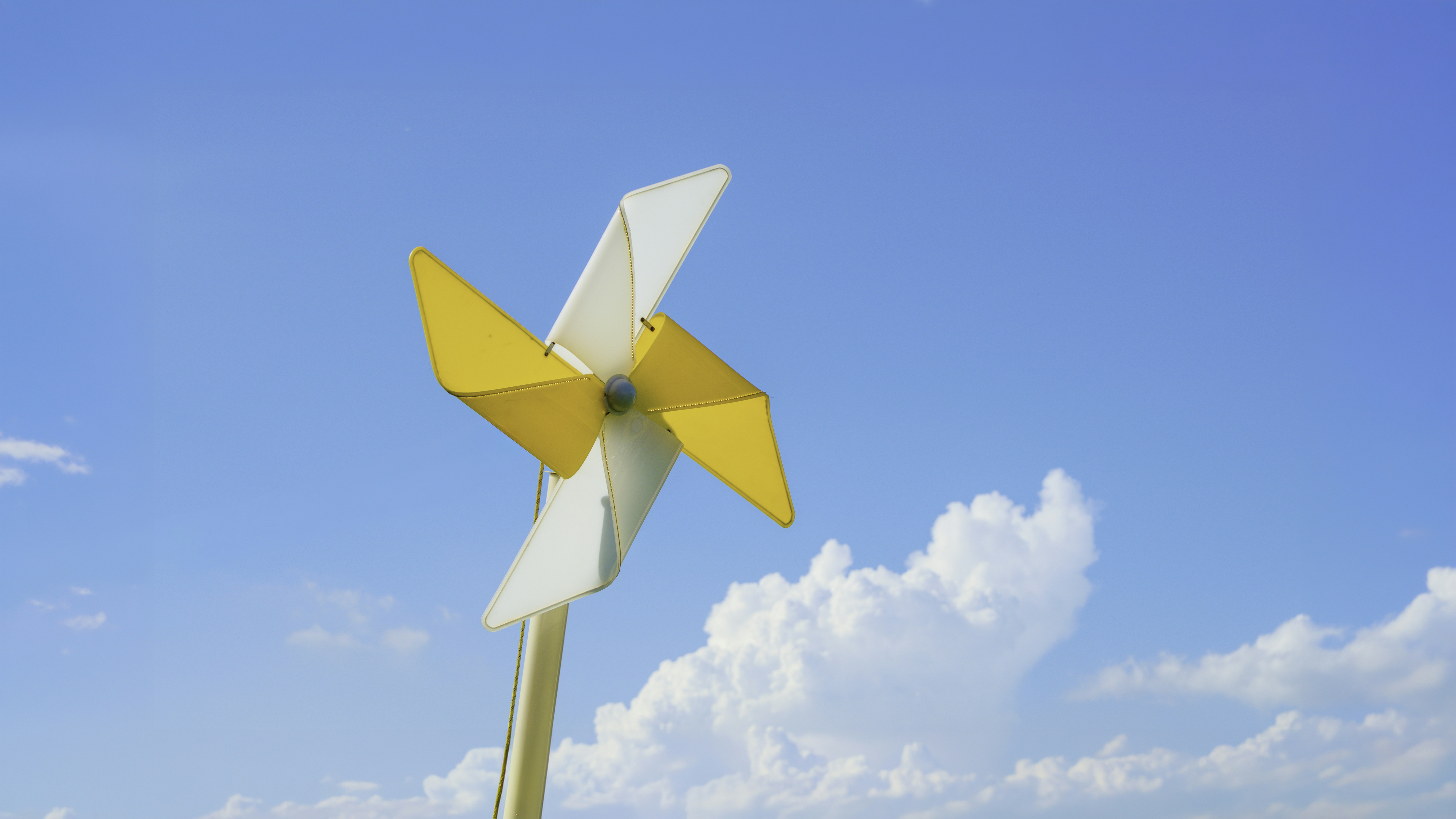 Un molinete amarillo y blanco contra un cielo azul brillante con nubes