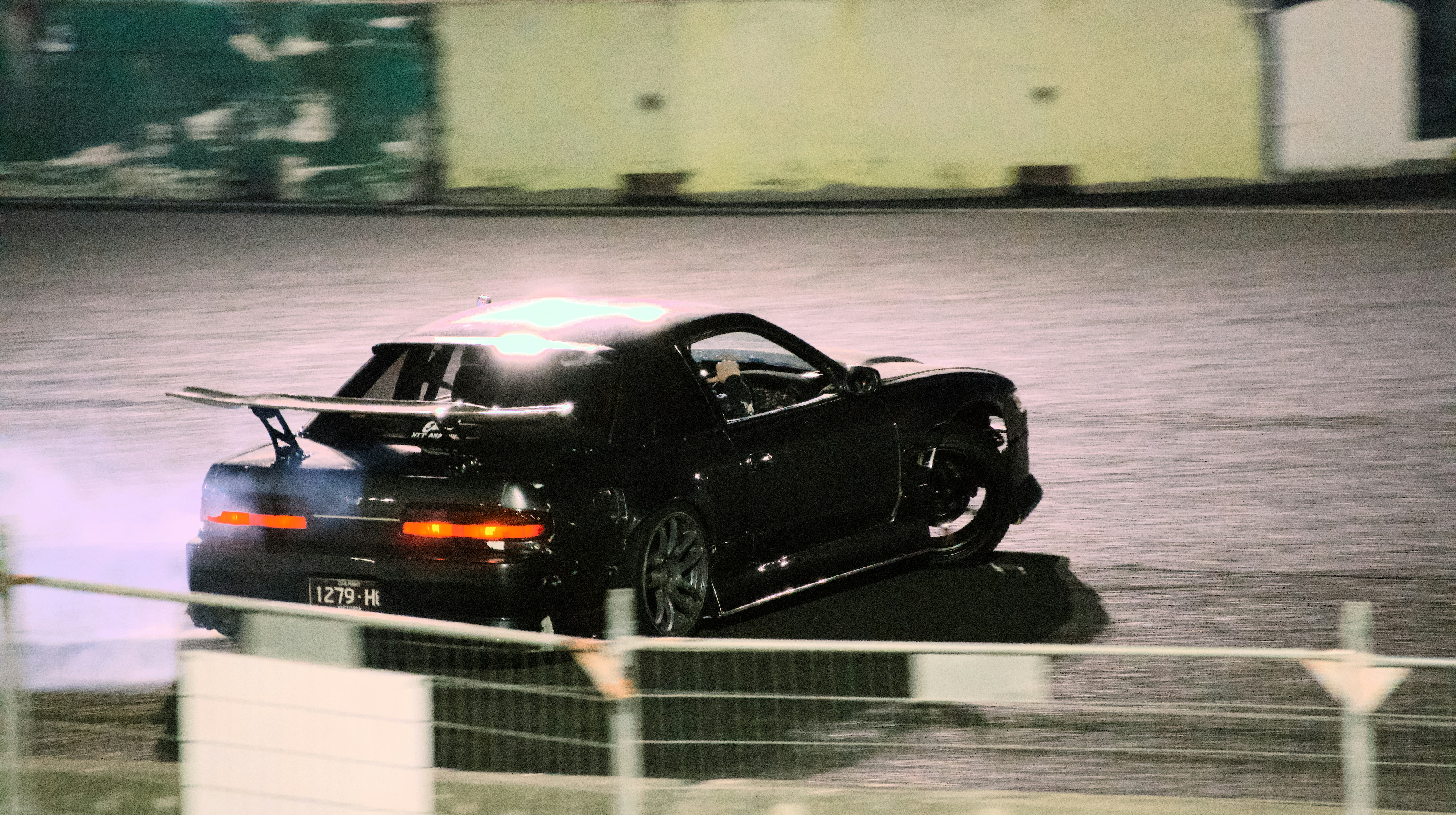 A black sports car drifting on a track at night with tire smoke