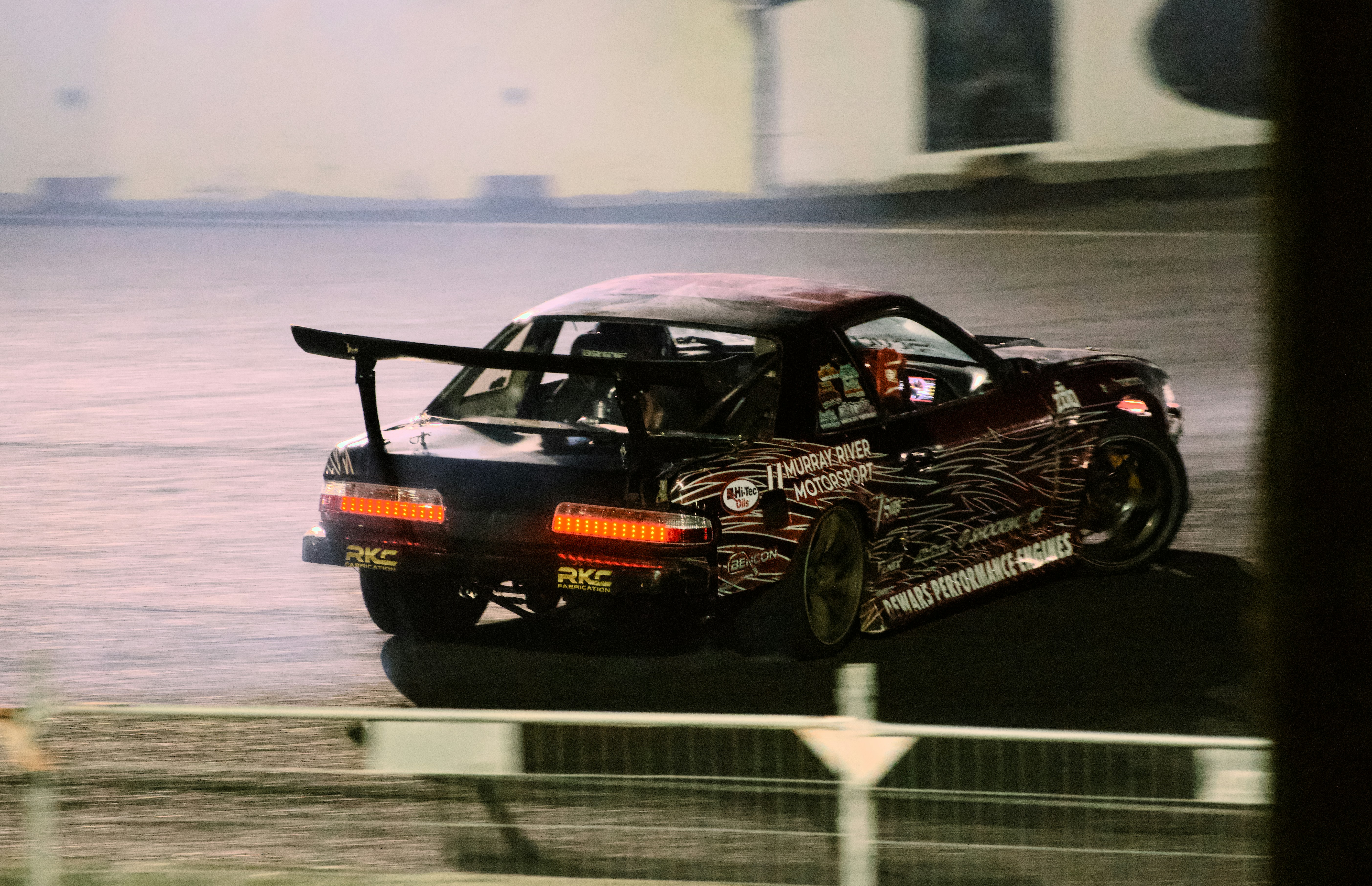 A dark drift car with a large rear wing sliding on a track
