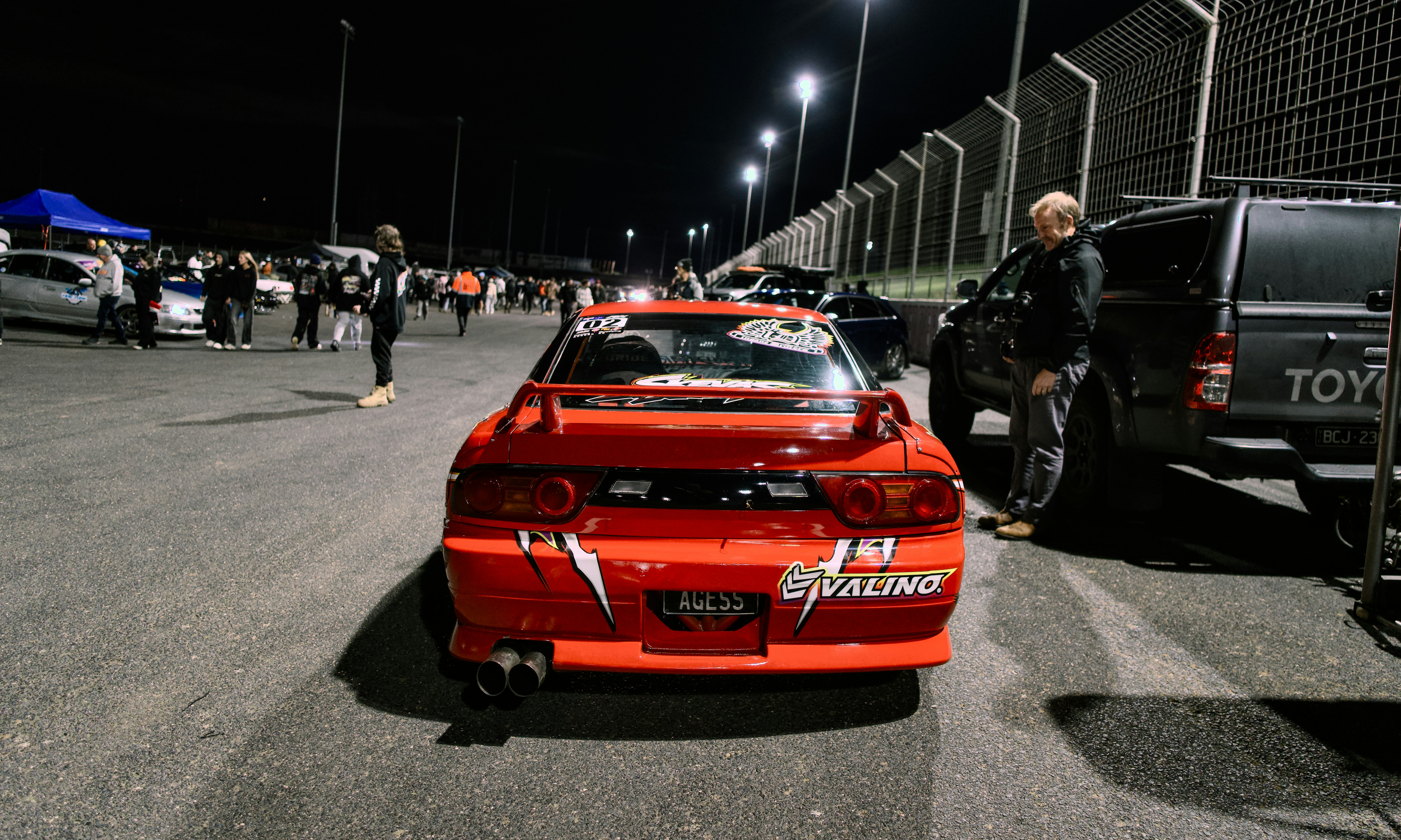 A red Nissan 180SX drift car parked in a night race track paddock