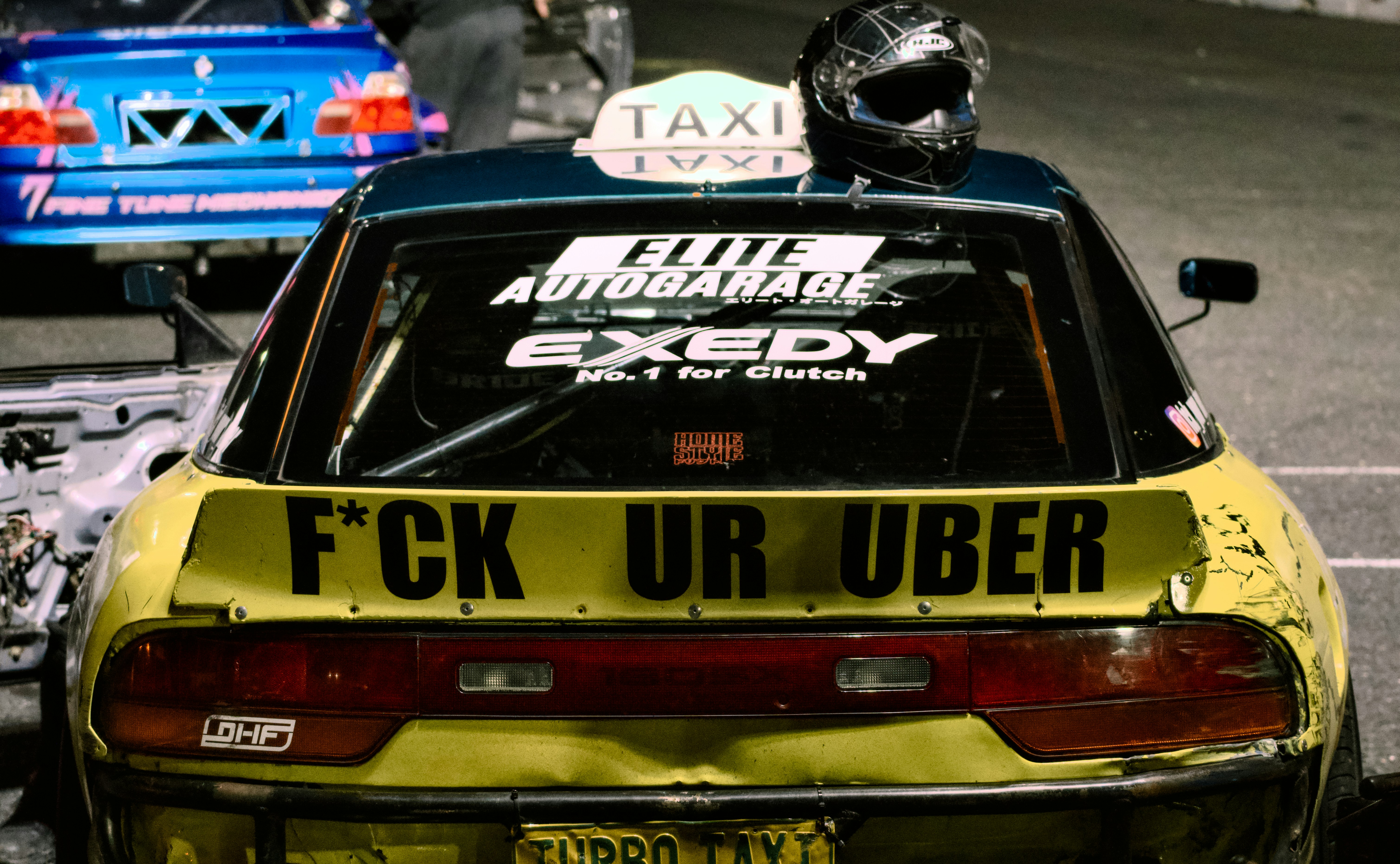 A yellow drift car with a taxi sign and helmet on the roof