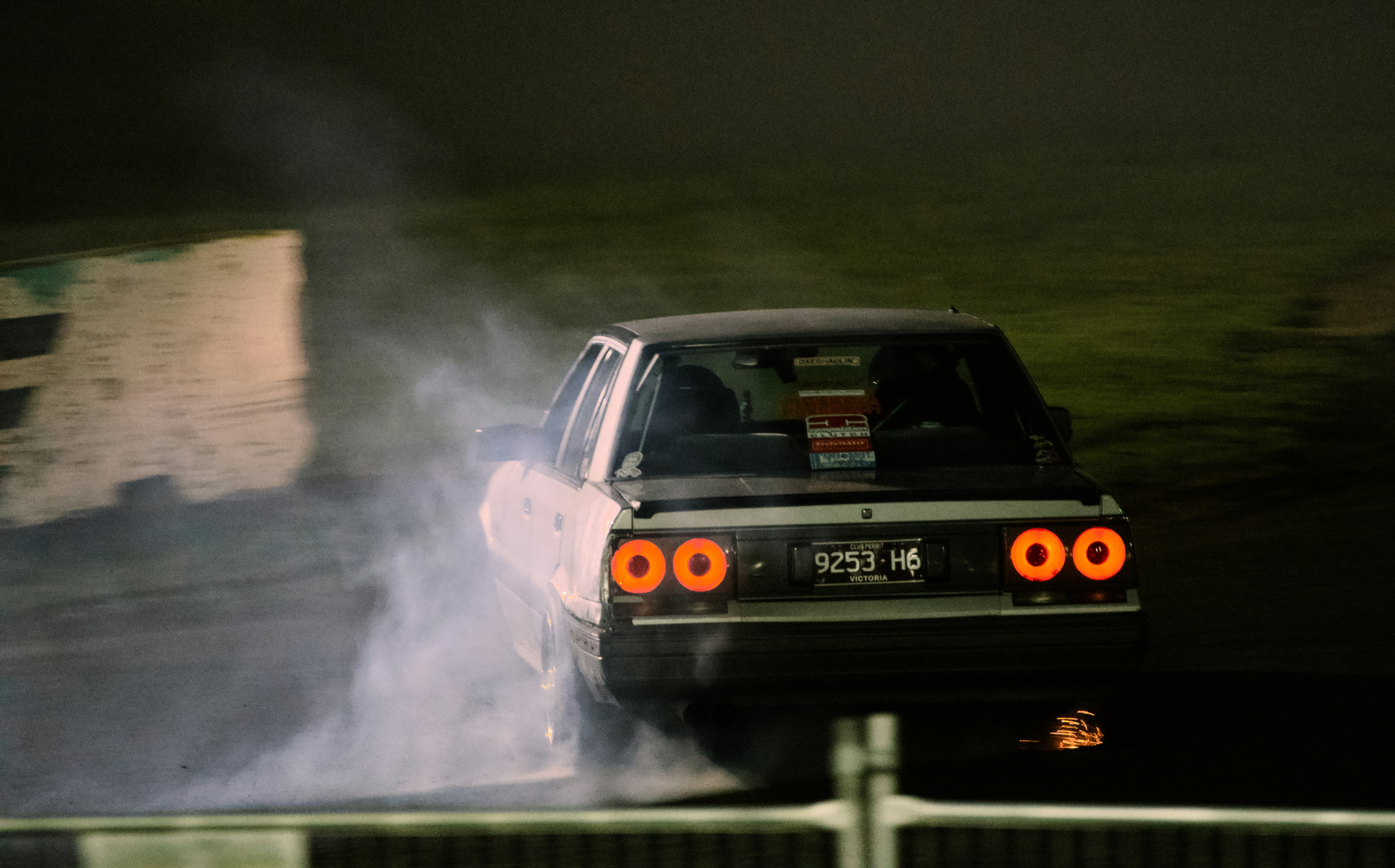 A car drifting on a track at night with smoke and glowing taillights