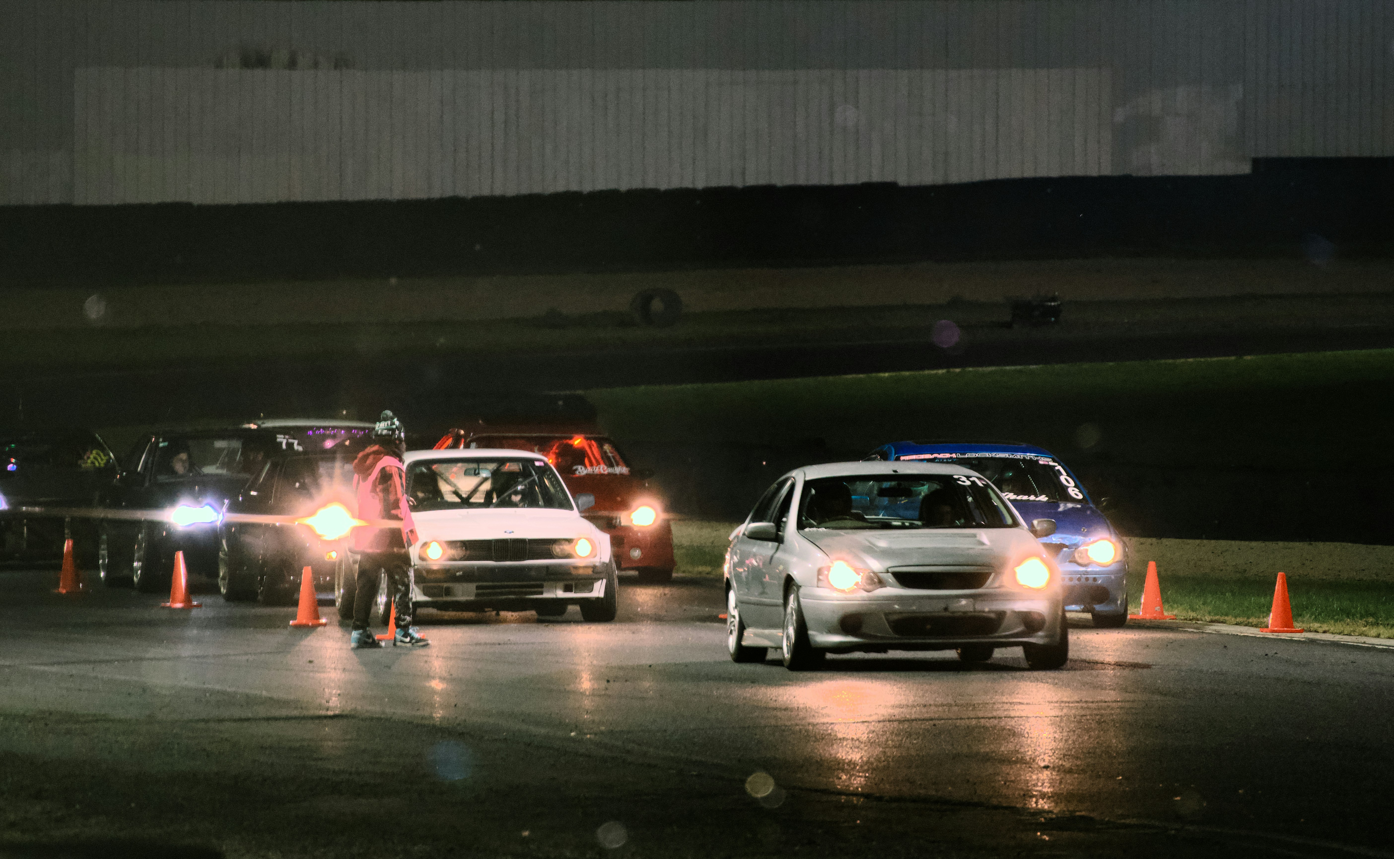 A person in a high-visibility vest directing cars on a racetrack at night