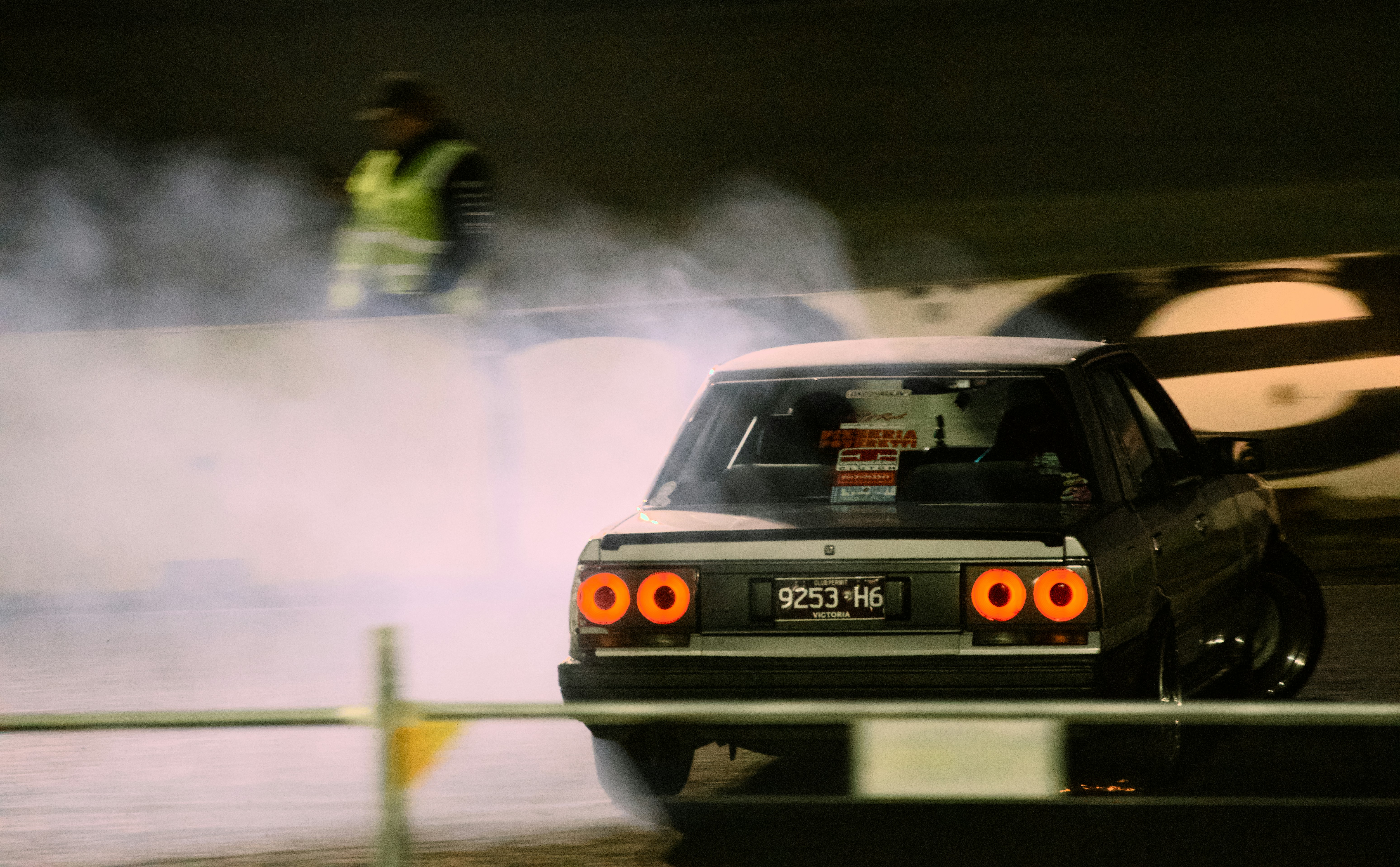 A silver car drifting on a track at night with thick tire smoke