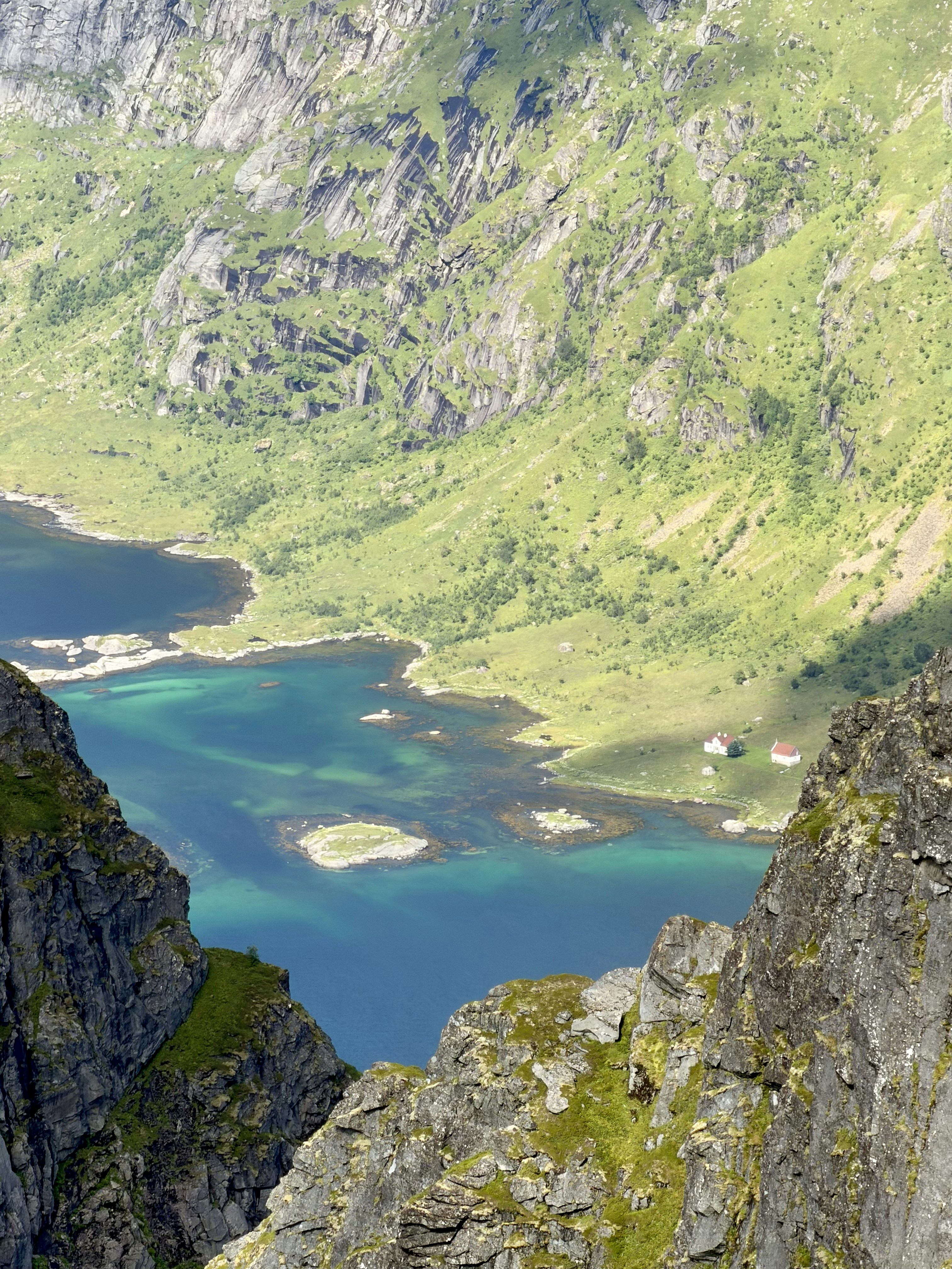 A turquoise fjord between steep rocky cliffs with two small houses on the shore