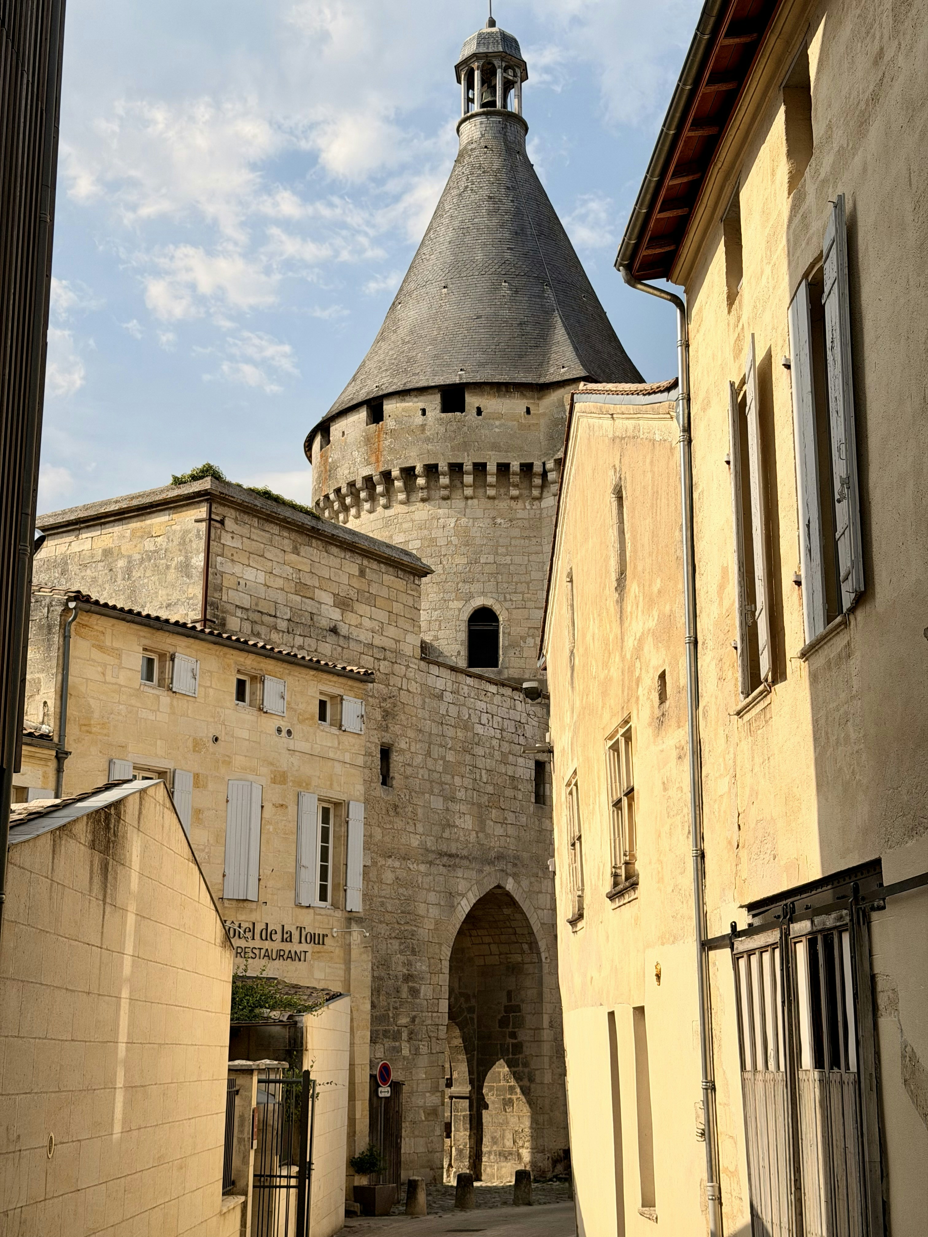 A stone medieval tower and arched gateway between yellow buildings in a French town