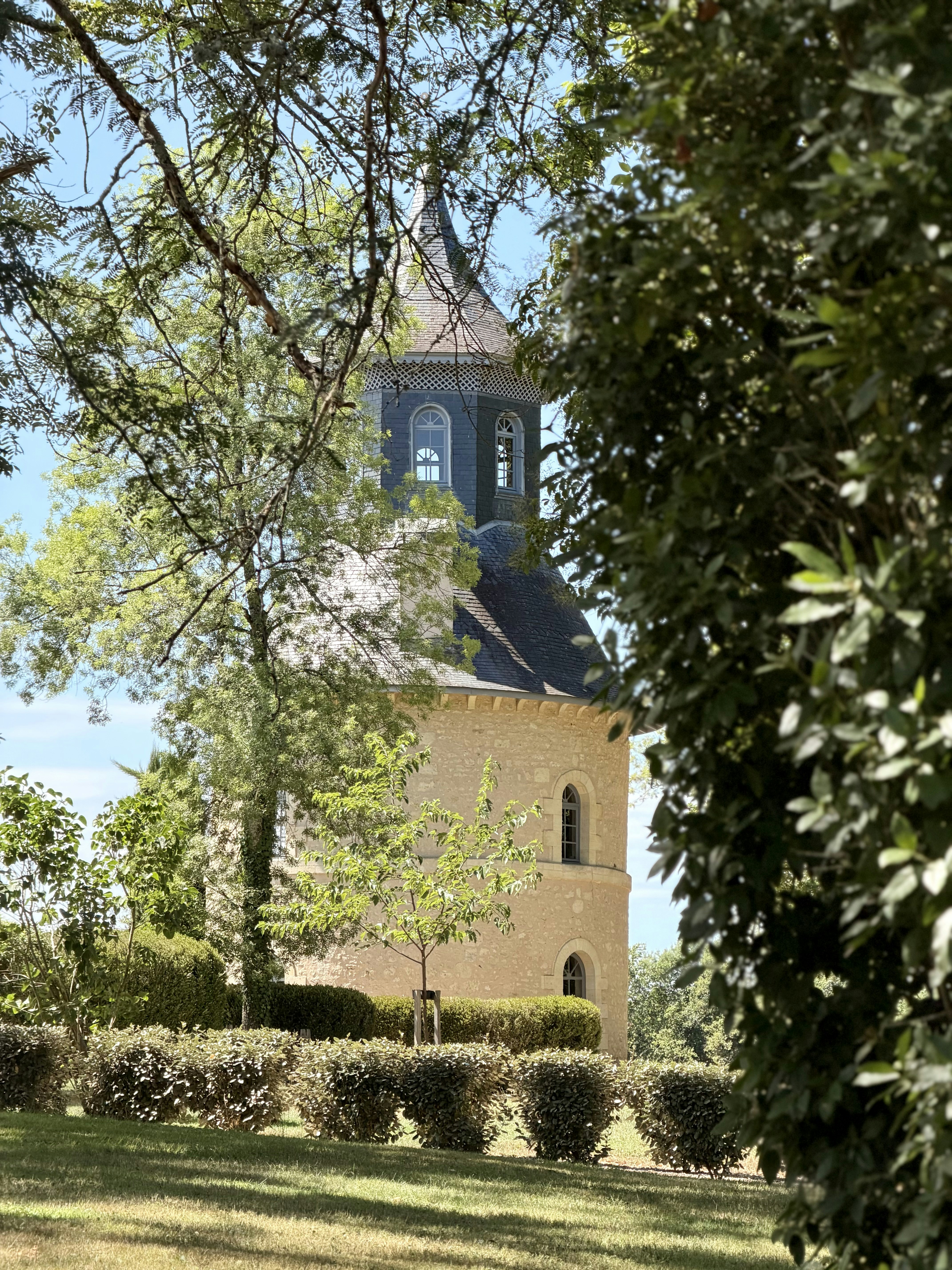 A stone tower with a conical roof behind manicured hedges in a garden