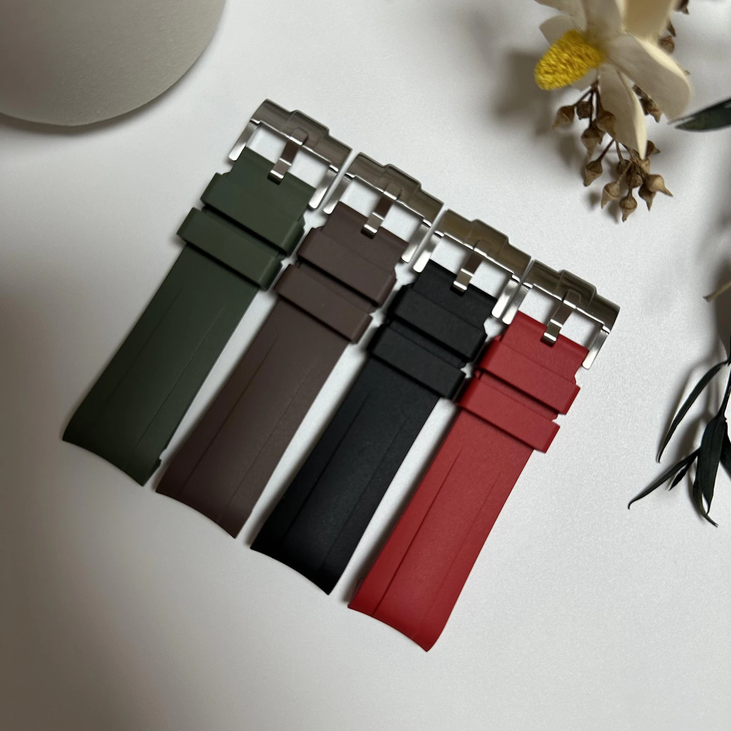 Four quick-release rubber straps in olive, brown, black and red with steel buckles on white