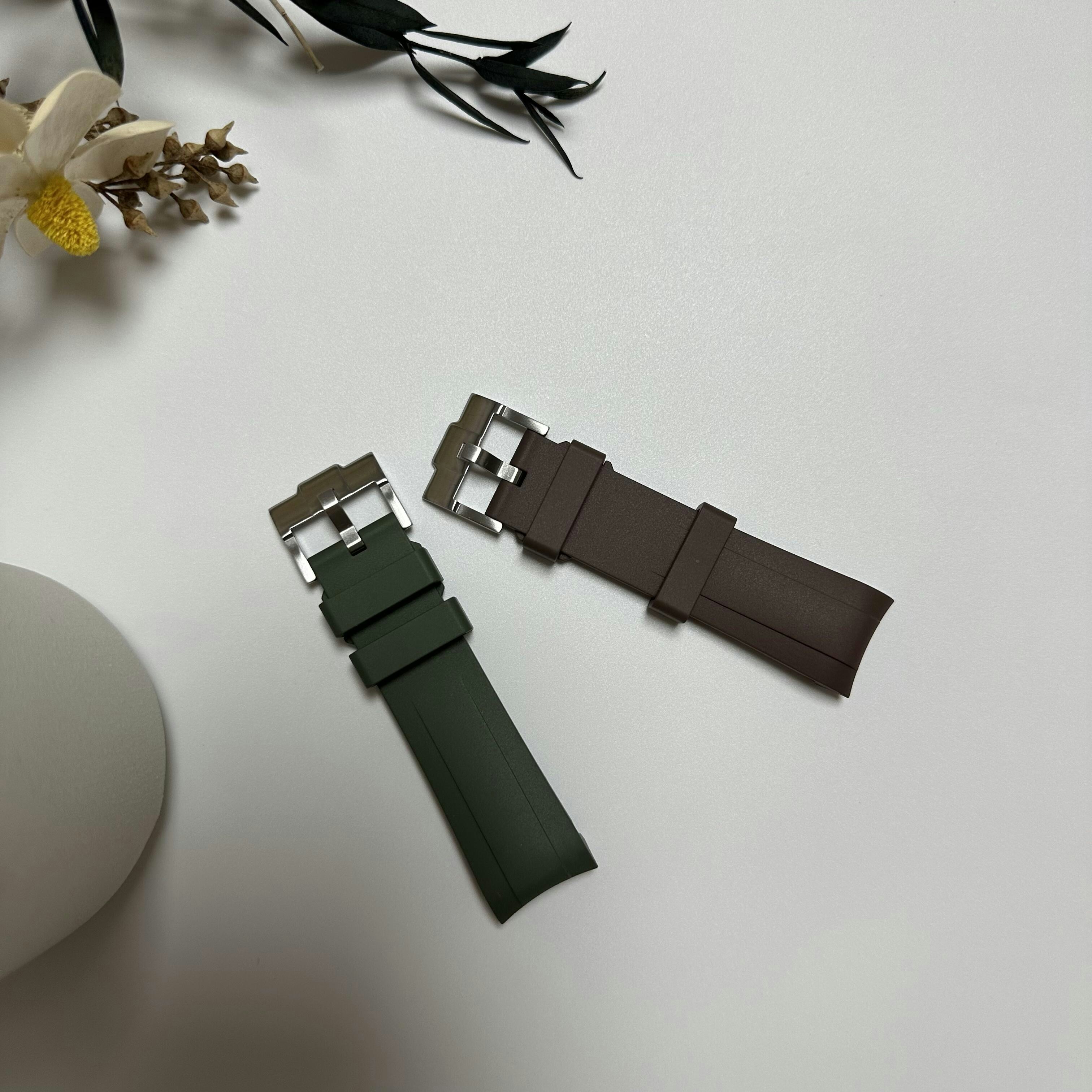 A green and a brown rubber watch strap with silver buckles on white