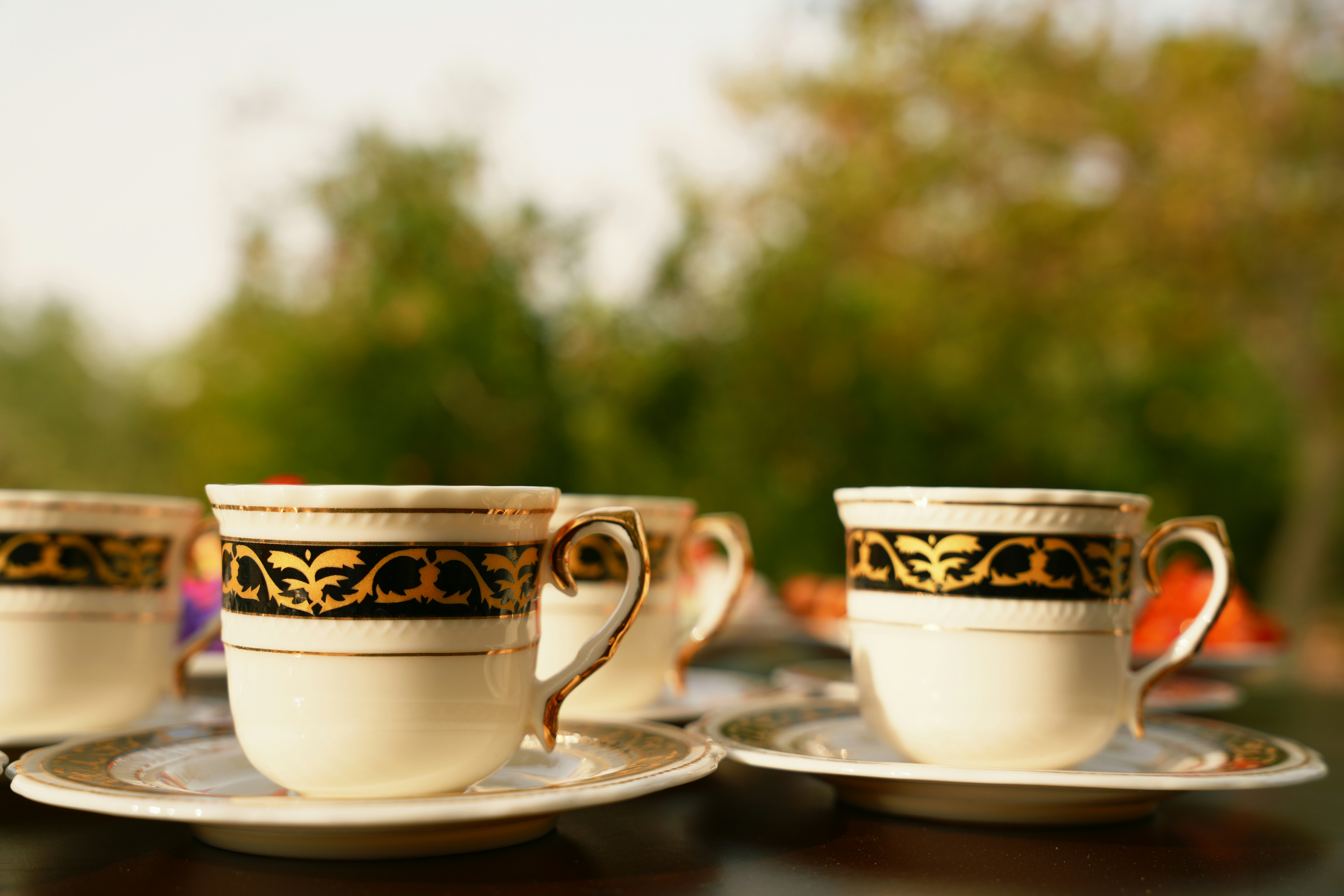 Three white porcelain teacups with gold and black ornate patterns on matching saucers