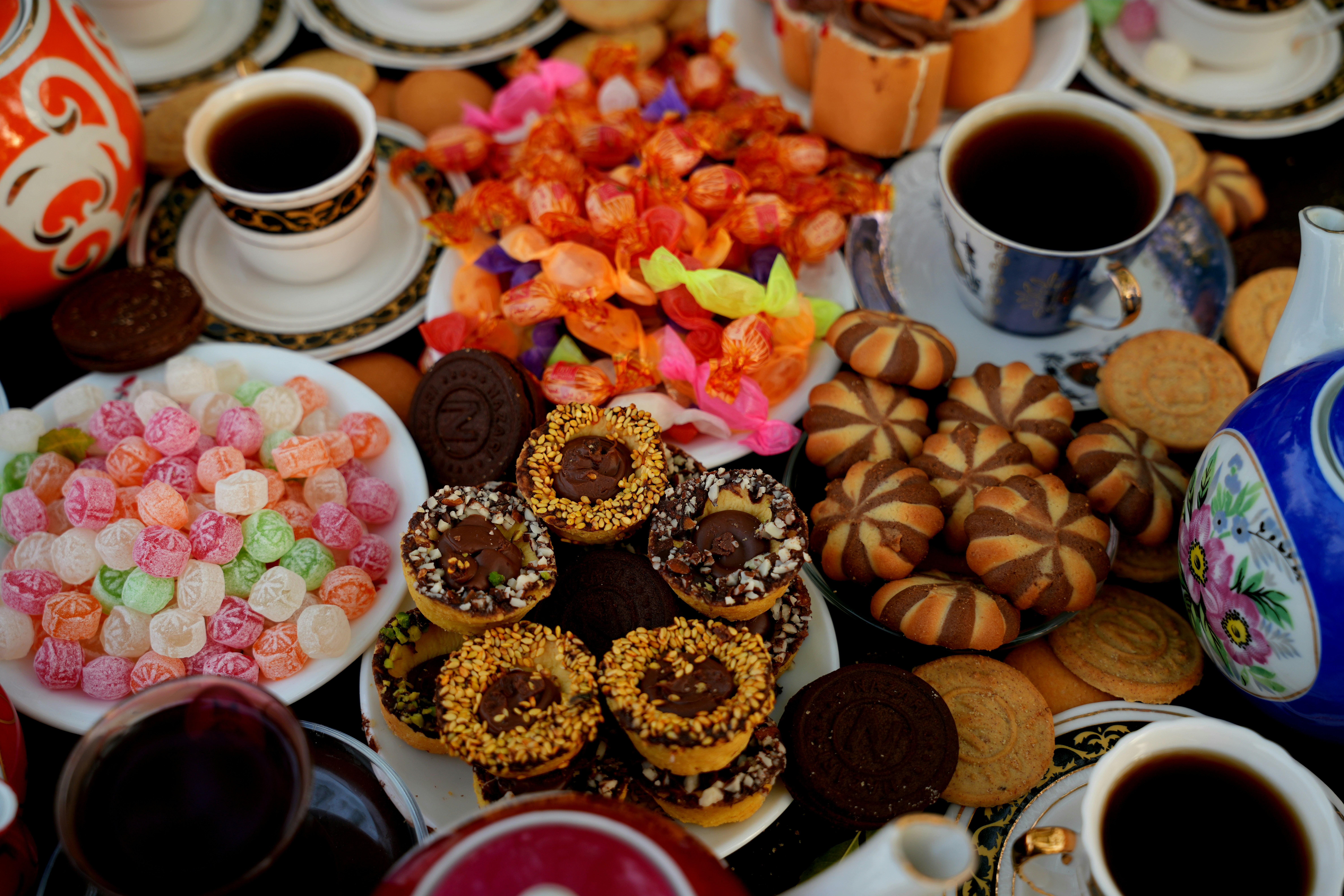 Assorted cookies, candies, and cups of tea arranged on a table for tea time
