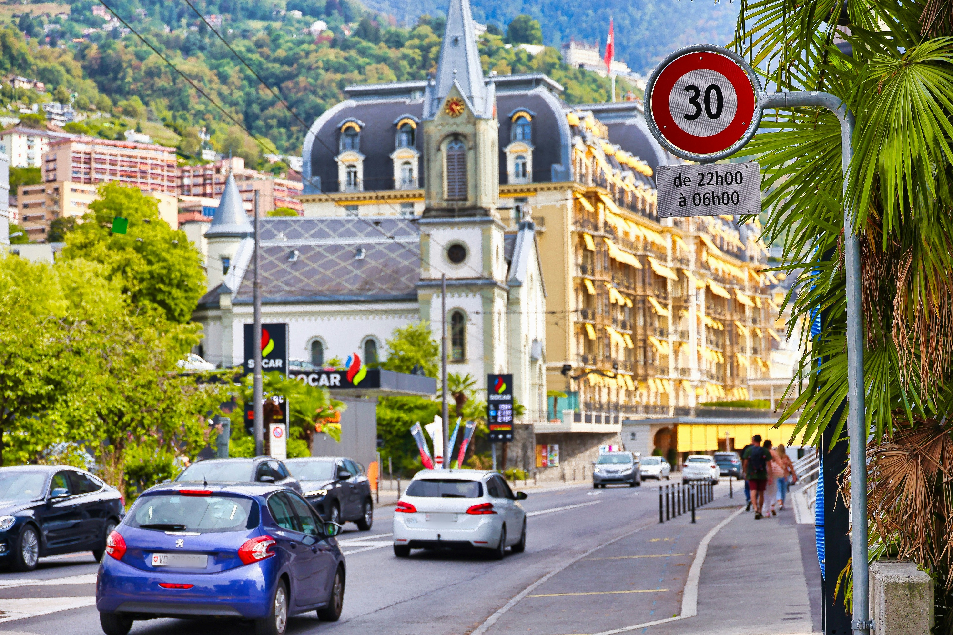 Cars driving on a street past a historic building and a speed limit sign