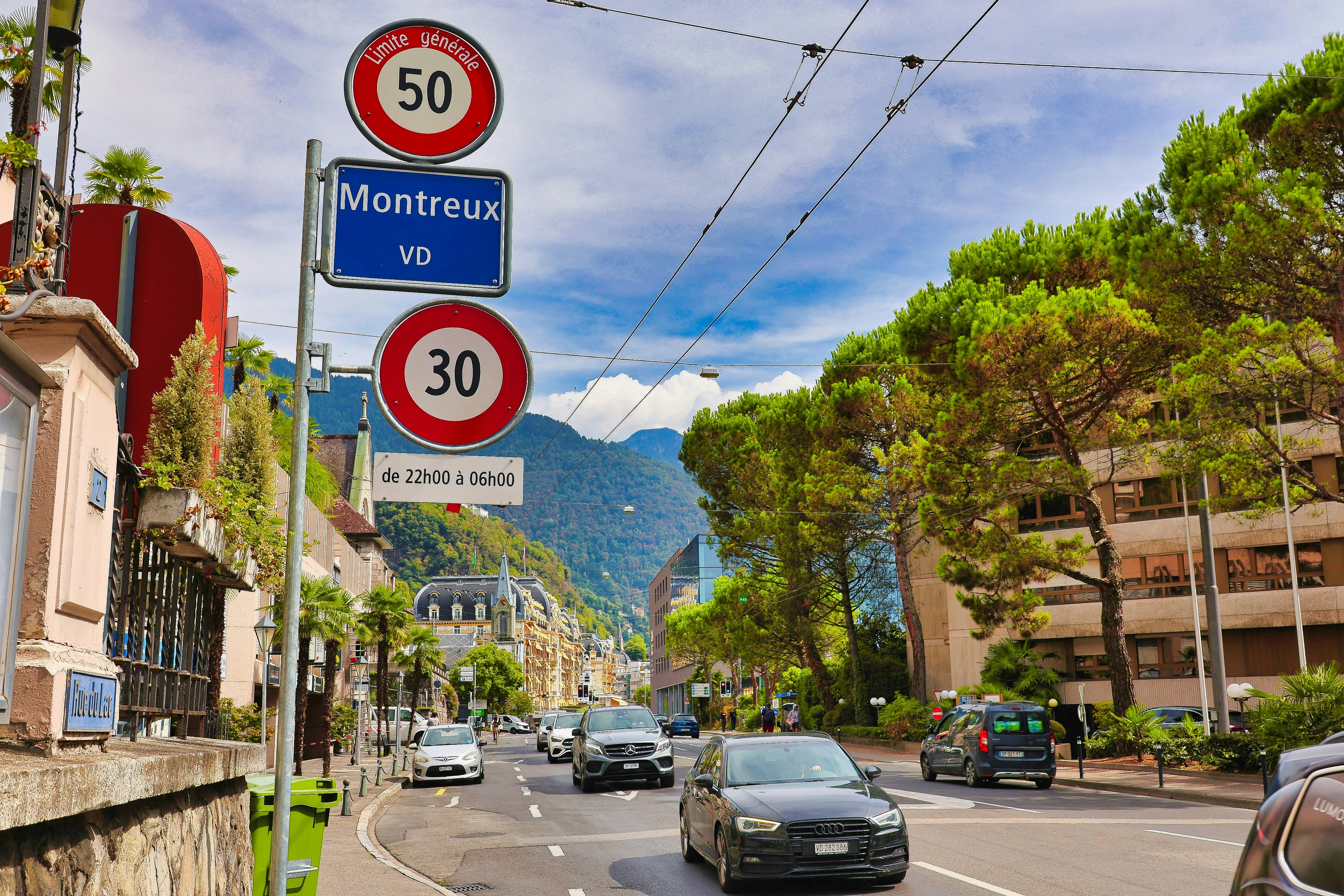 Traffic signs for Montreux in Switzerland above a street with cars and pine trees