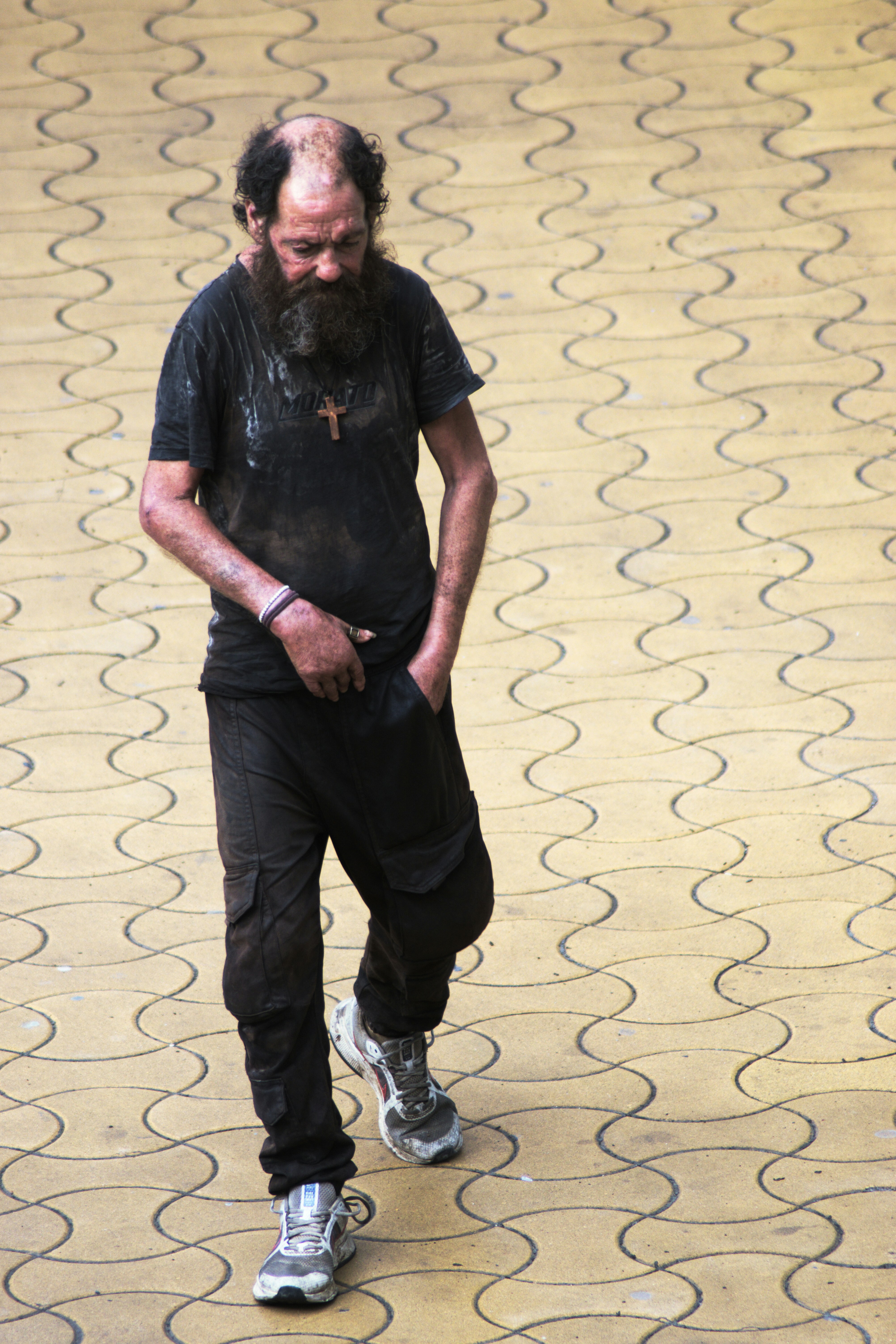 A man with a beard and a wooden cross necklace walking on yellow pavers