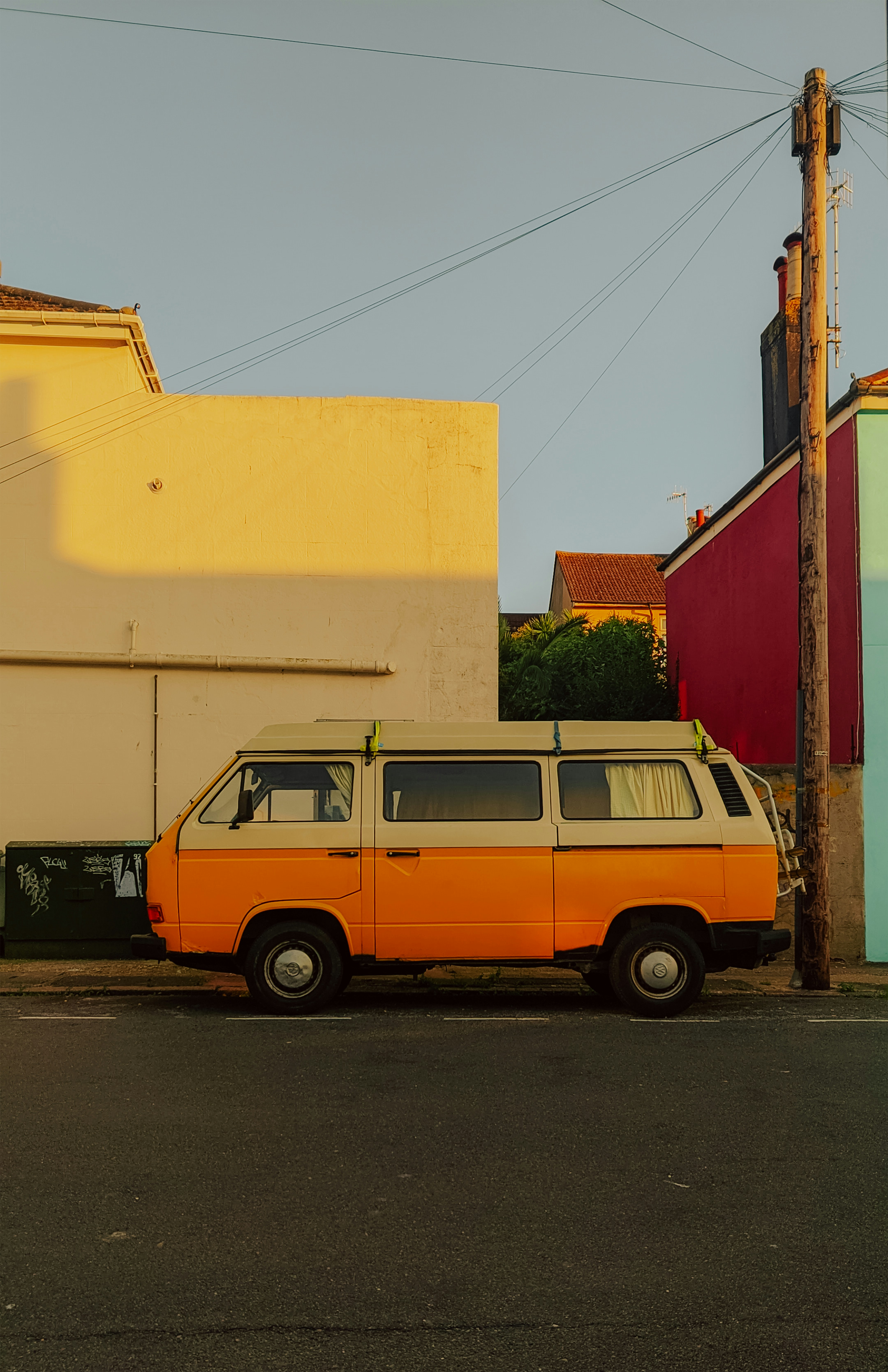A vintage orange and white Kombi parked on a street beside colorful buildings