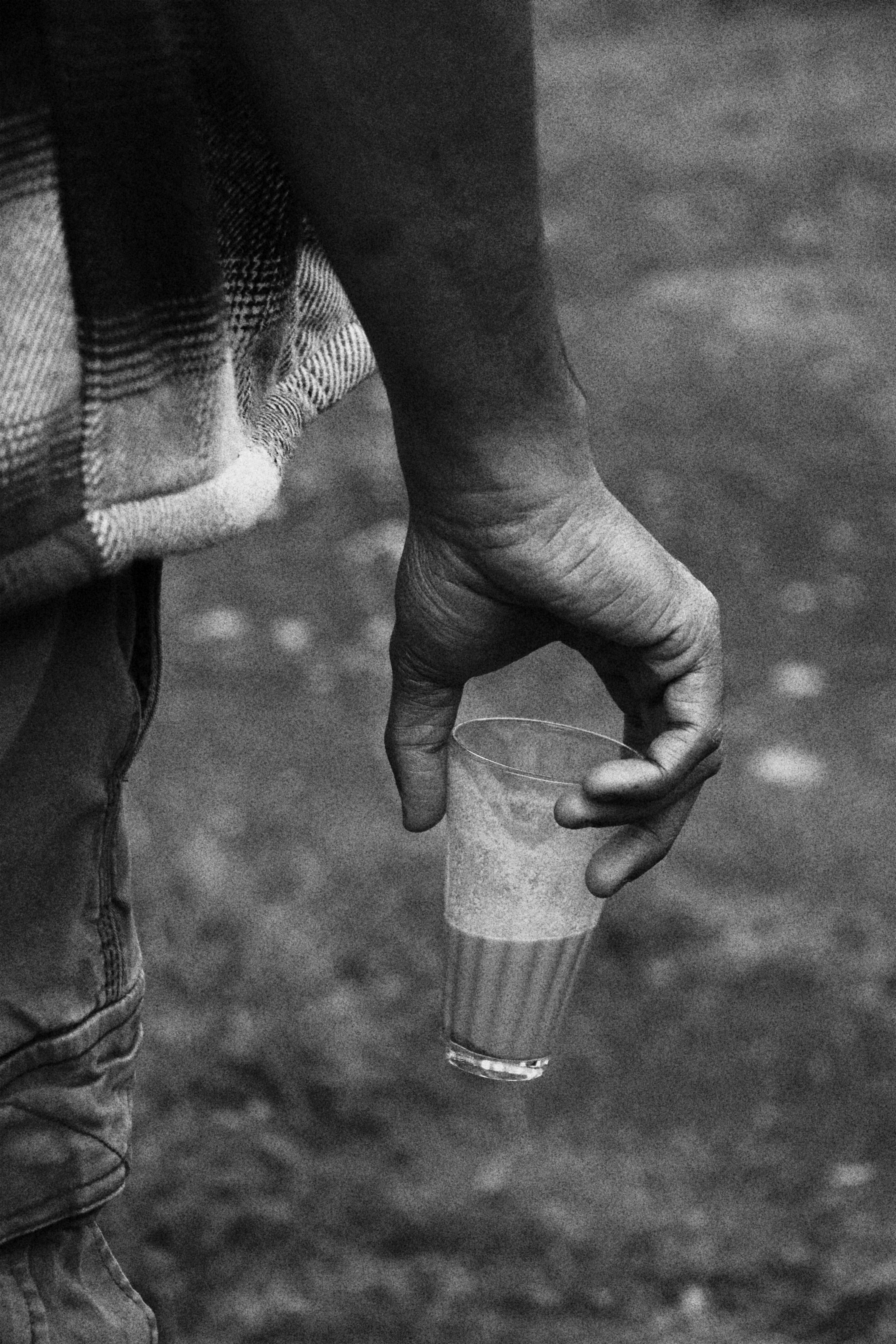 A person in a plaid shirt holding a small glass of tea