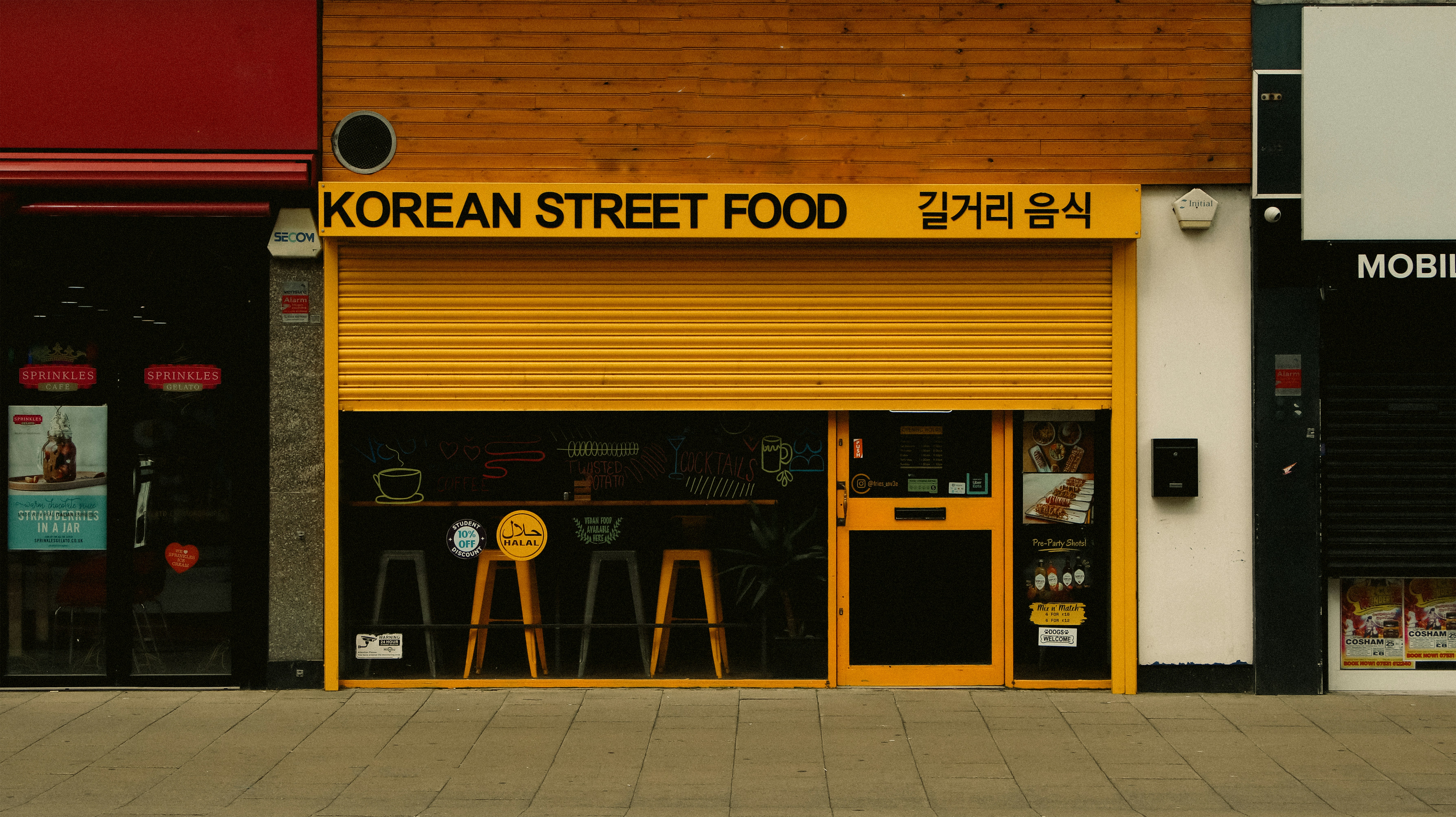 A closed Korean street food shop with a yellow metal shutter and stools