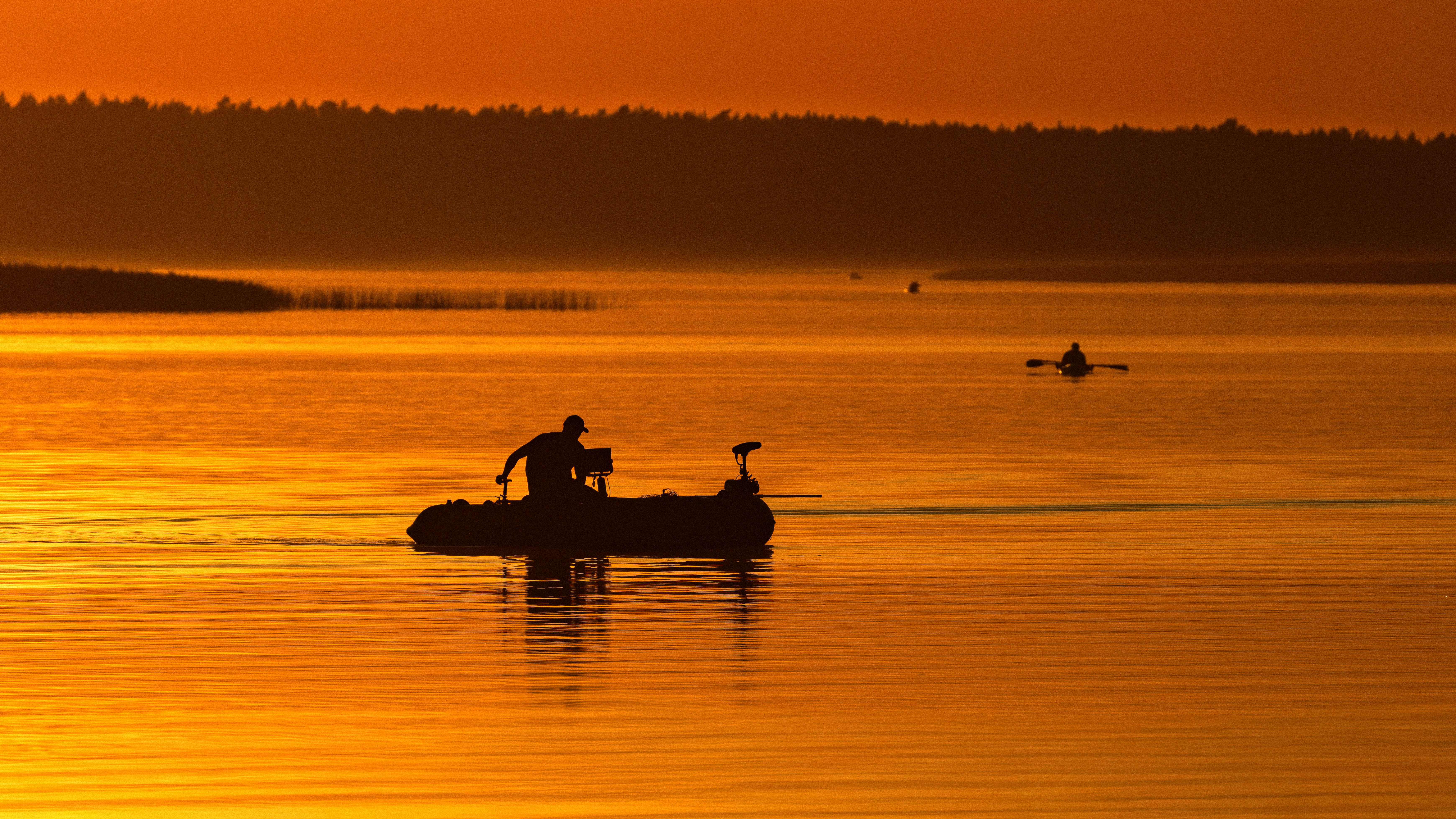 Silhouettes of people in small boats on a lake during golden hour