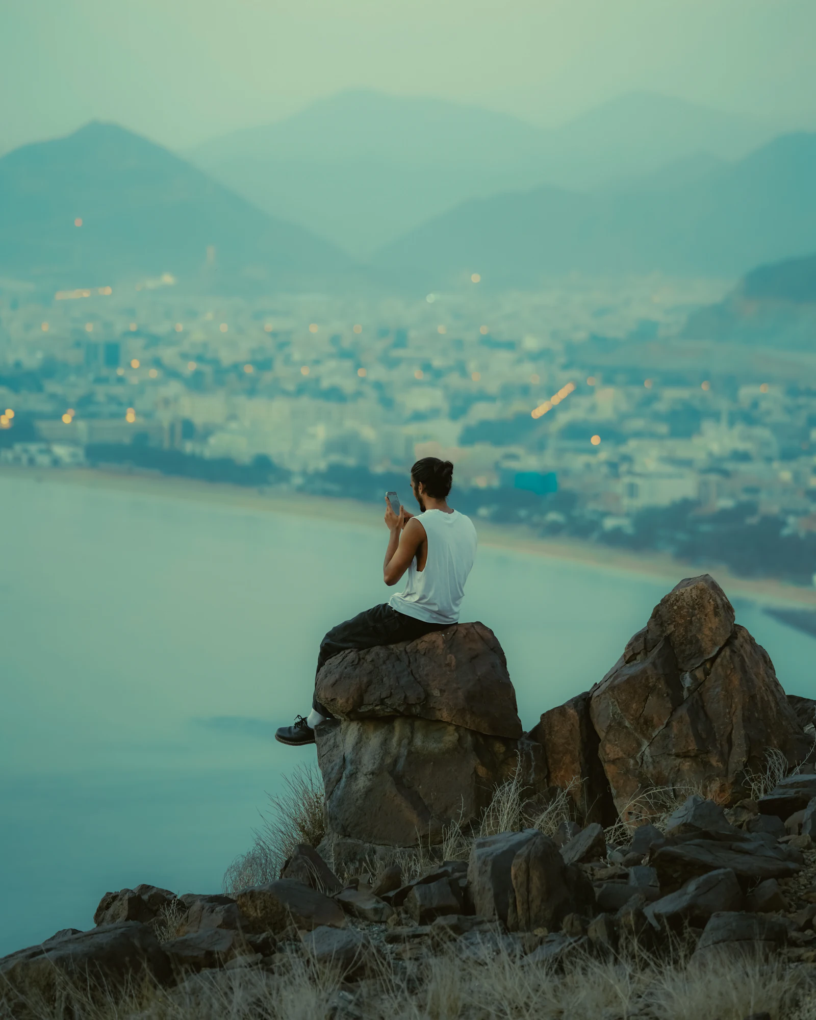 Traveller sitting on a rocky lookout above a coastal city, using a phone connected to a travel eSIM