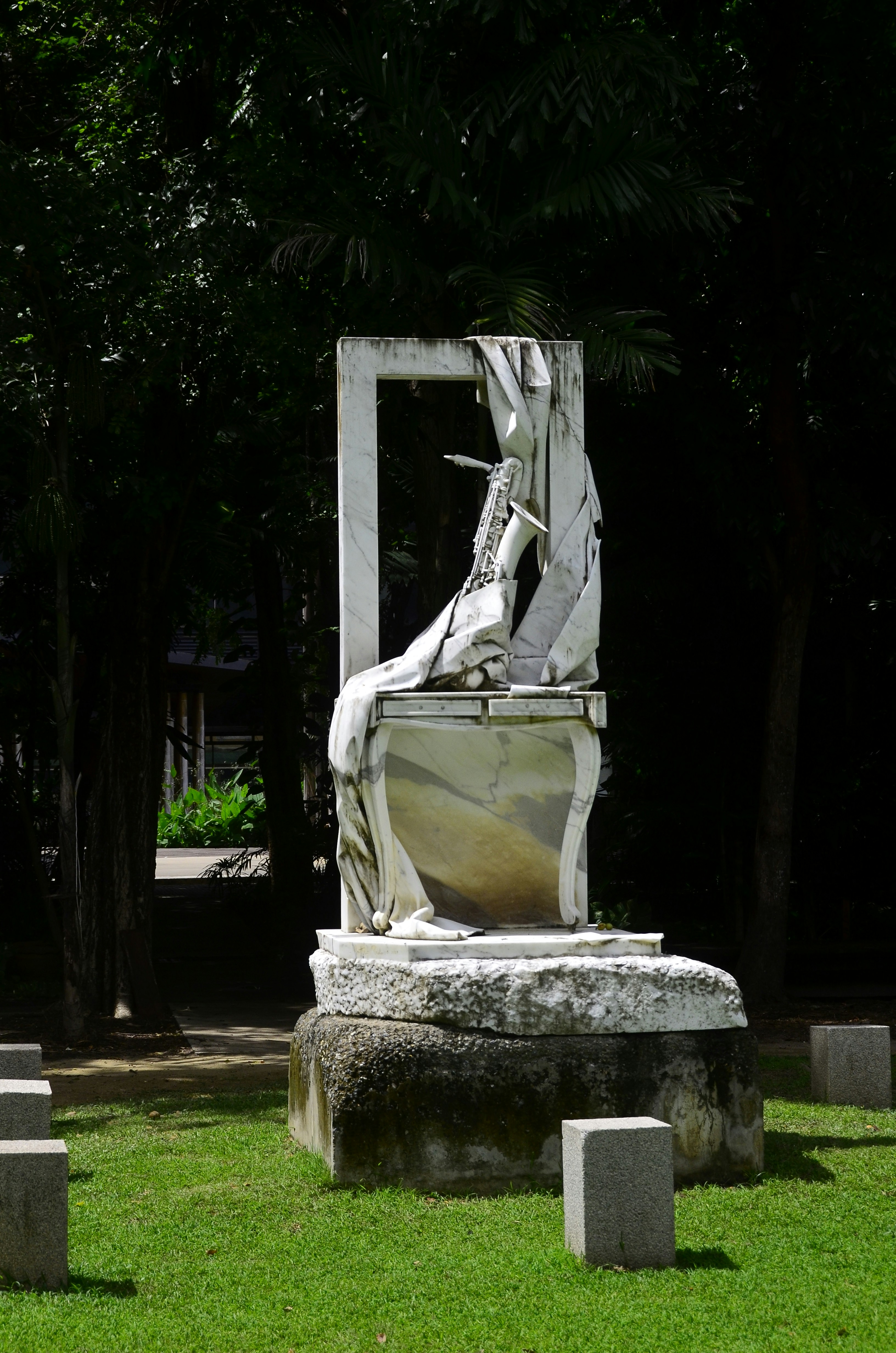 Una scultura in marmo bianco raffigurante un sassofono drappeggiato in tessuto su una base di pietra