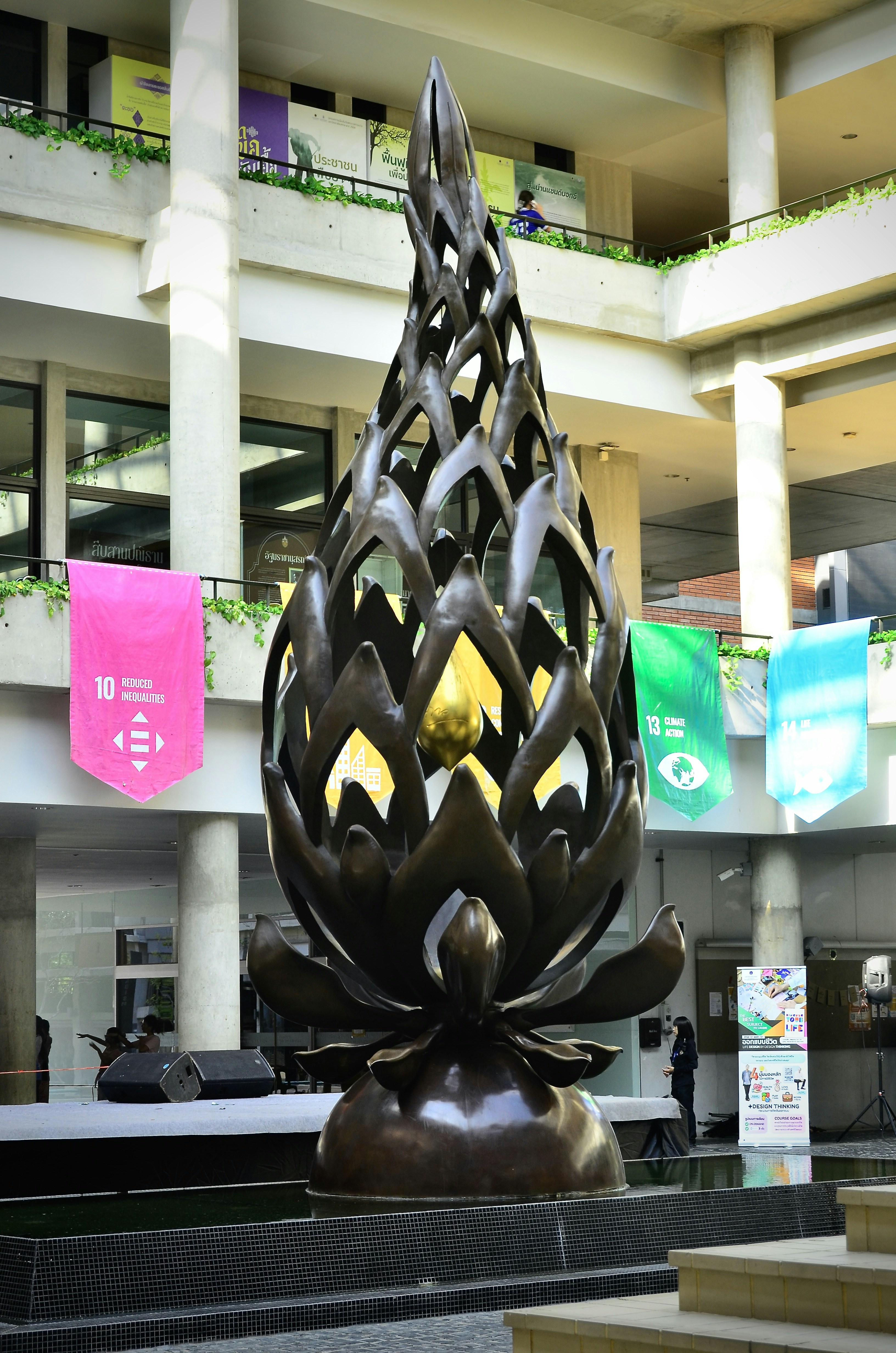 A large bronze lotus sculpture in an open-air atrium with colorful banners
